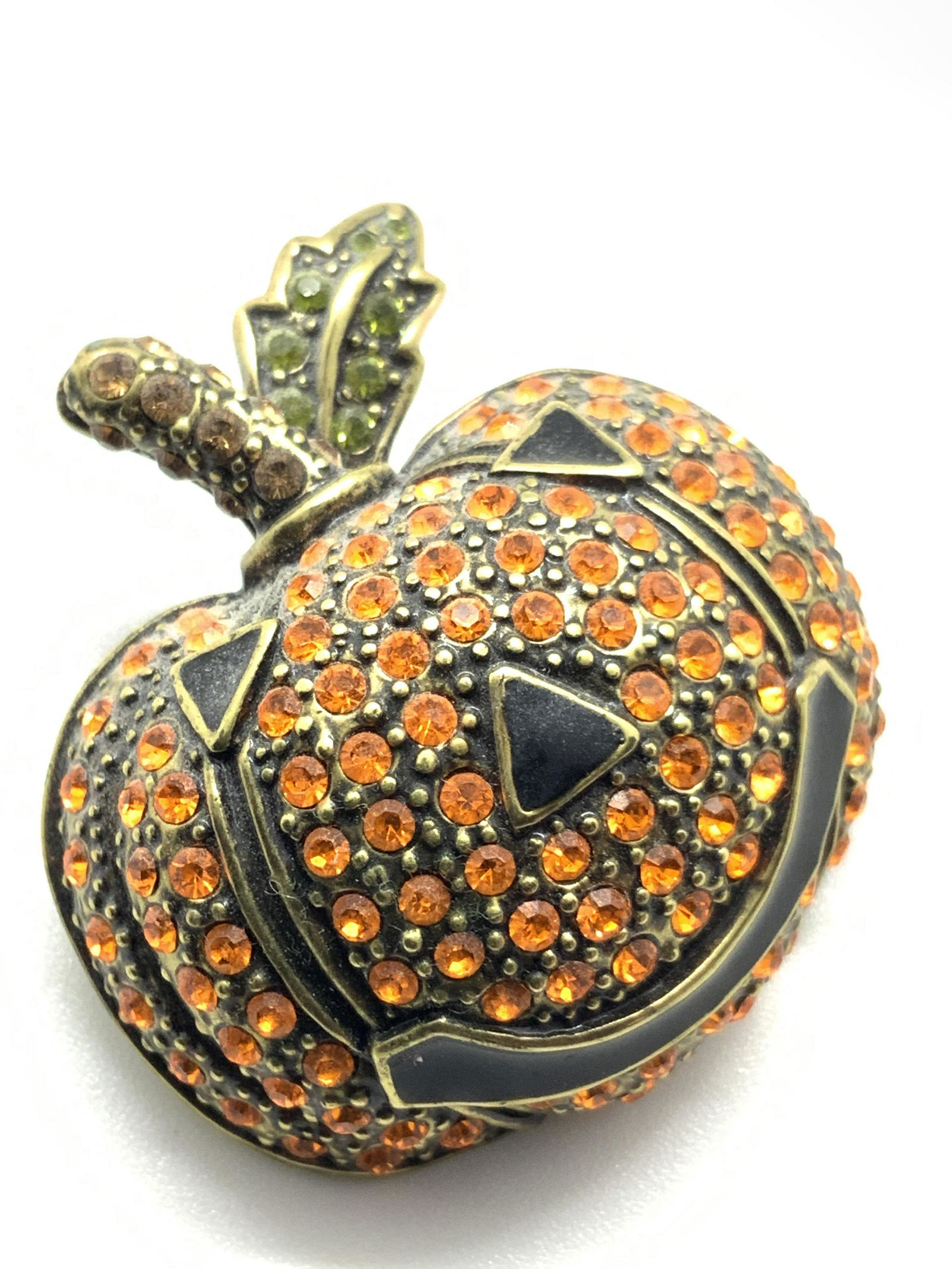 HEIDI DAUS Crystal Jack O‘ Lantern Brooch, Jewelry: A pumpkin form brooch with classic enamel Jack O’ Lantern features. Pumpkin is all orange crystals. It’s stem has light orange crystals. The leaf attached to the stem has green crystals. Underside
