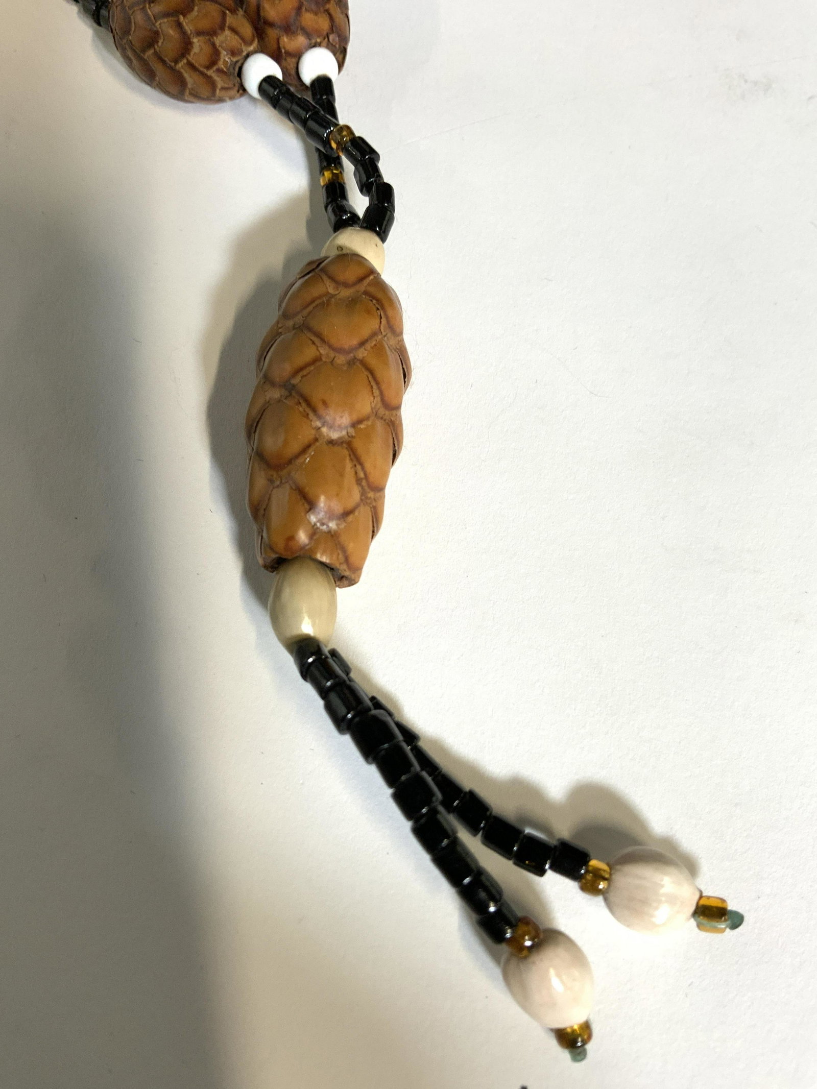 PINECONE BEADED ARTISANAL NECKLACE Jewelry: Unique Unisex necklace with Oversize 1 in. pinecone beads flanked with white beads and set apart with black beads. Ends in a pinecone pendant with bead tassel, app 3.75 in. L. Necklace length app 28 i