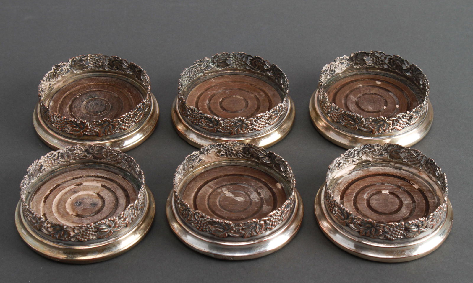 English Sheffield Silver-Plate Coasters Set of 6: Set of six English Sheffield silver-plate on copper and wood coasters, pierced grapes and leaf motif, hallmarked. 1.25" H x 3.25" diameter.
