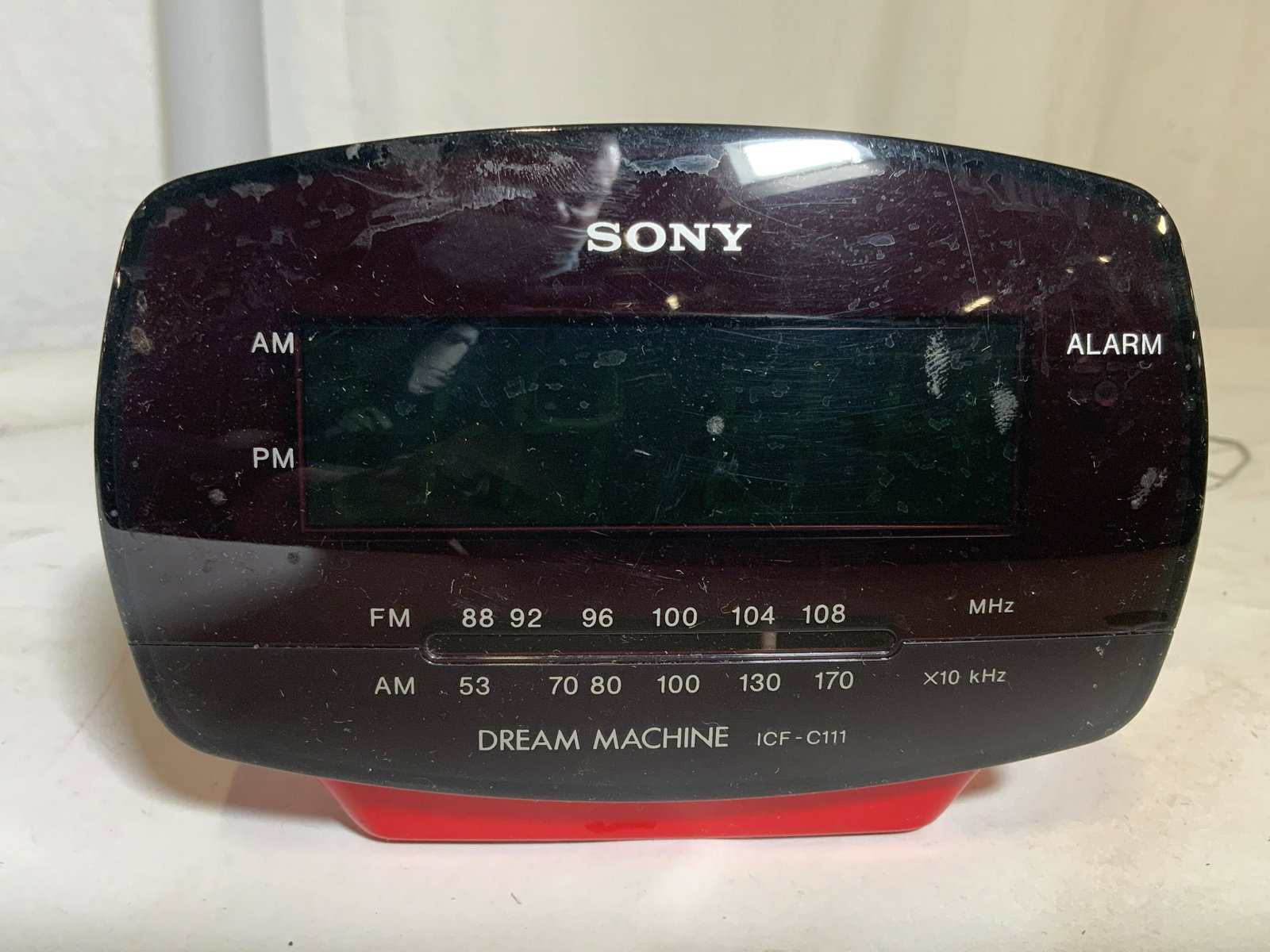 SONY DREAM MACHINE ICF C111 Alarm Clock: Front of piece is marked SONY DREAM MACHINE ICF C111. Piece is red toned. Top of piece has on & off switch, clock button, time set buttons, alarm & sleep buttons. Left side has speaker. Right side has