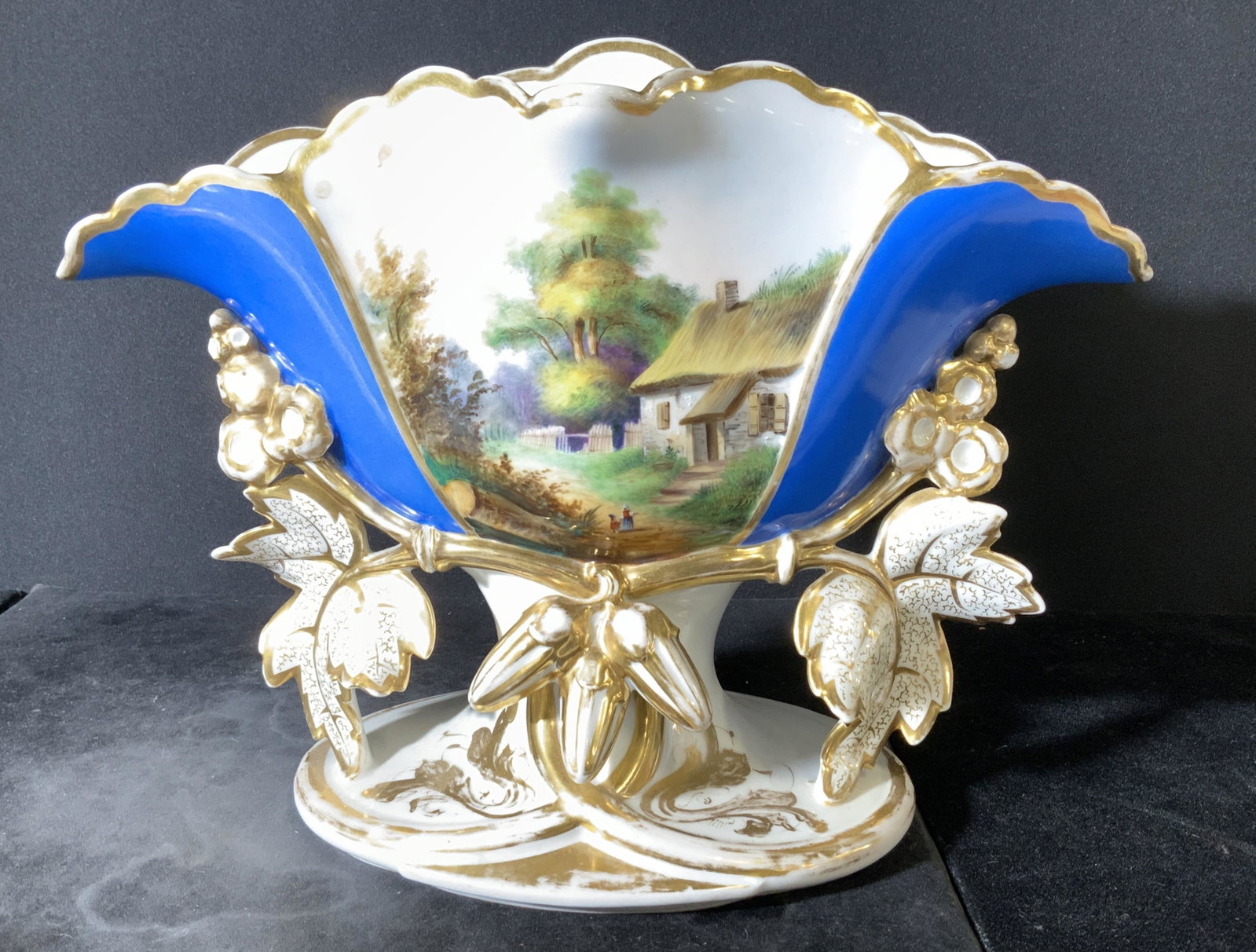 Gilt European Vintage Centerpiece Porcelain Vessel: Rococo style Hand painted scenery of farmer’s thatched straw roof home in countryside, flanked by rich blue color and gilt outlining all around. Stark white porcelain vessel on short pedestal with p
