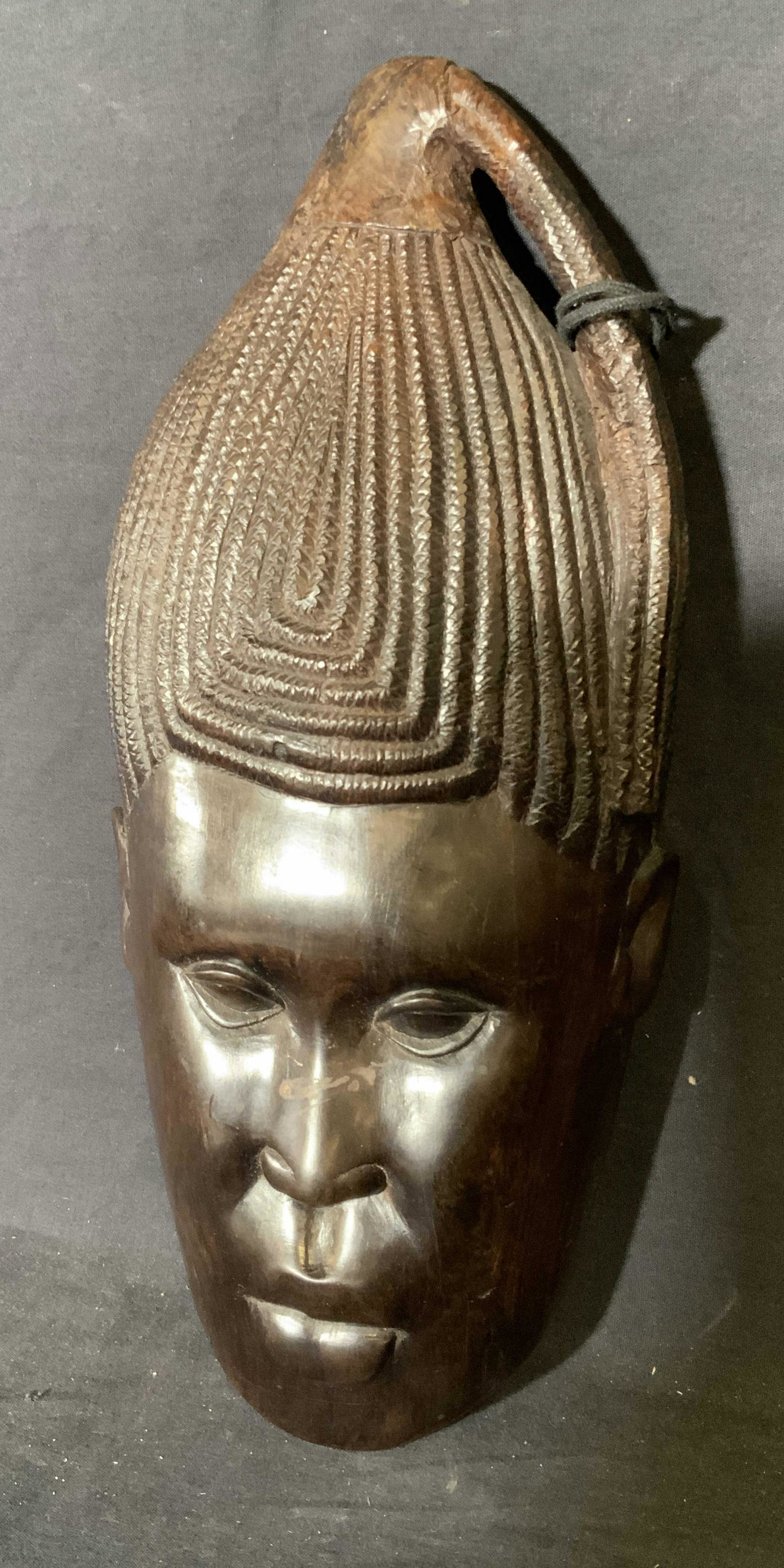 African Wooden Mask: African wooden mask, no apparent inscriptions or markings, wooden nail taped to reverse, mask displays an elongated face with a mass of braided hair, piece measures 14.5 inches tall by 6 inches wide, 