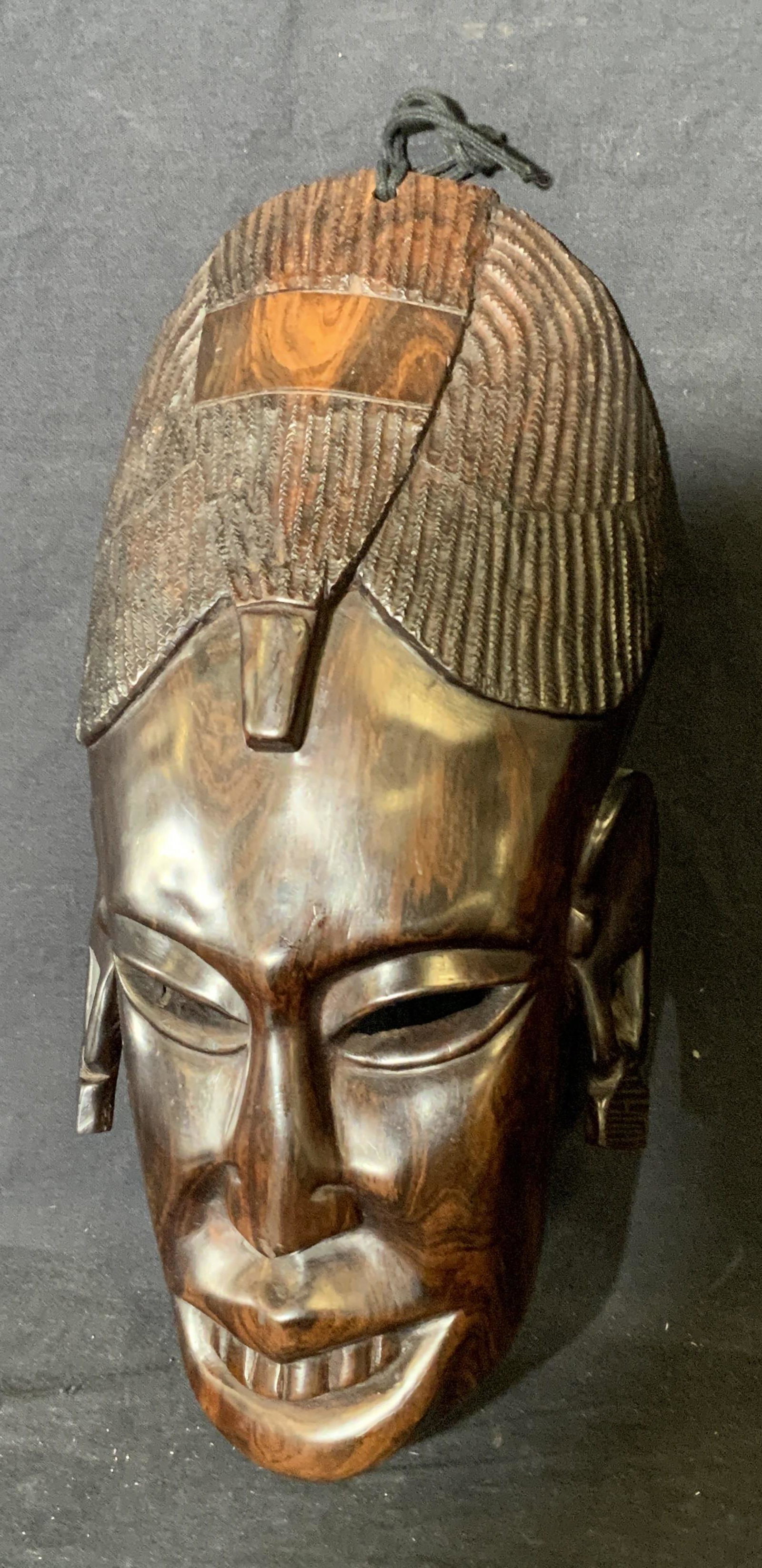African Wooden Mask: African wooden mask, no apparent inscriptions or markings, wooden nail taped to reverse, mask displays an elongated face in a grin with a mass of braided hair and square earrings, piece measures 13.5 