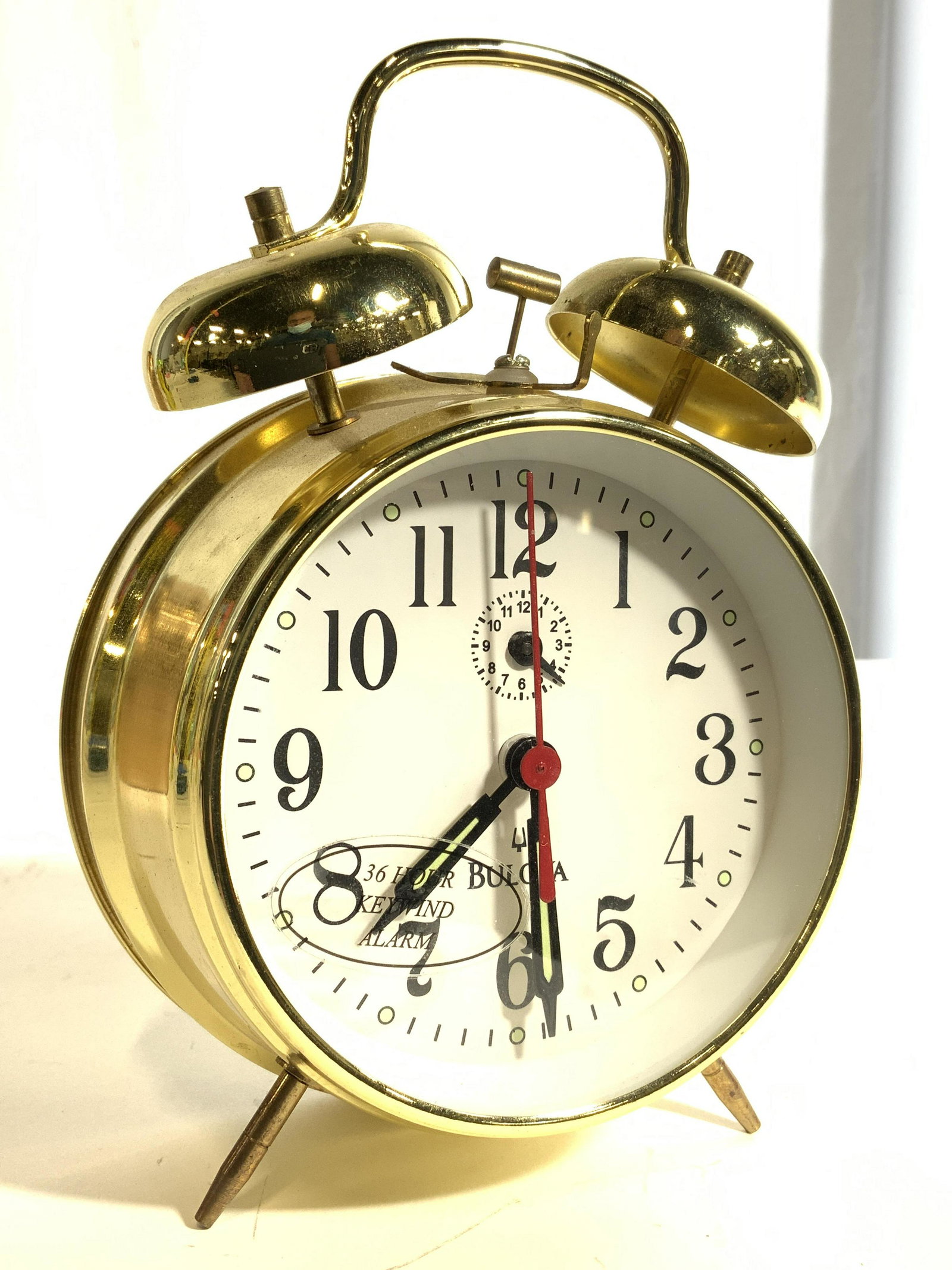 BULOVA 36 Hour Keywind Alarm Clock: Clock face reads BULOVA. Tag on front reads 36 HOUR KEYWIND. Clock is gold toned and metal. Clock face is white with black numbers. Piece has 2 feet & 2 bells on top. Piece measures approx 7 inches ta