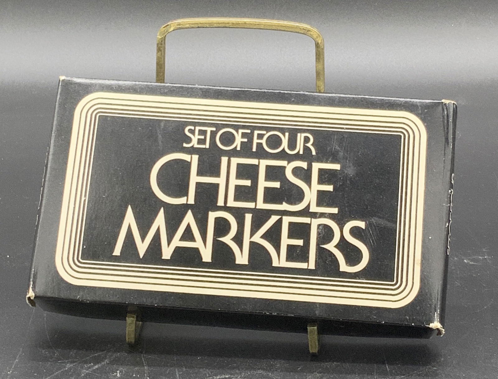 Set 4 KNOBLER Porcelain Cheese Markers, Org Box: Four white porcelain cheese markers in their original box. Pieces appear to have not been used. Each piece reads THIS CHEESE IS:. Some wear to the lettering. Underside has a sticker that reads KNOBLER