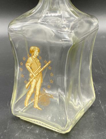OLD FITZGERALD COLLECTION Glass Liquor Bottle: A colorless glass liquor bottle impressed on the underside: OLD FITZGERALD COLLECTION LIQUOR BOTTLE, 65 4 69. The lid is a gold toned composite material with a cork style stopper. The image of a man h