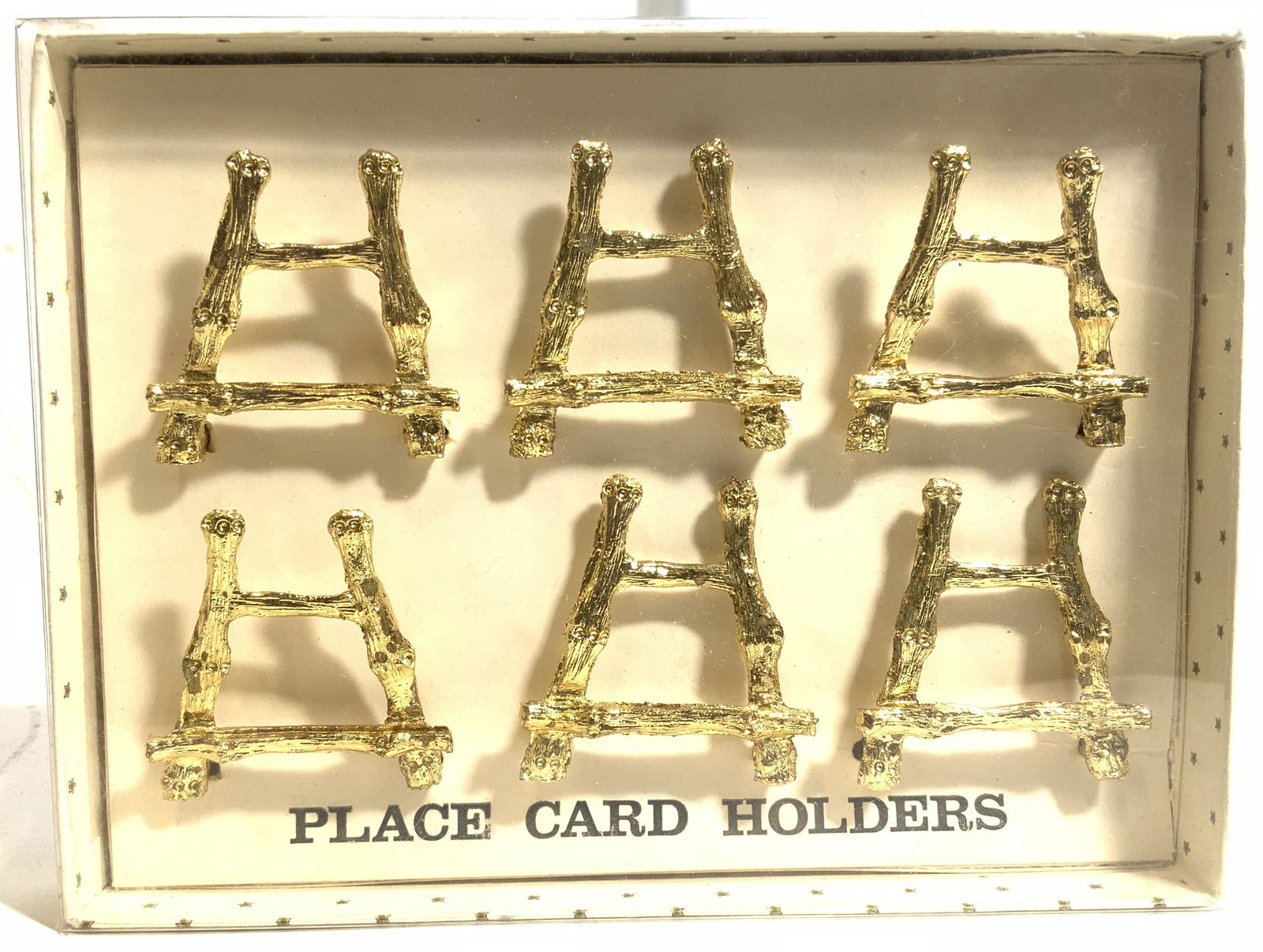 Set 6 Gold Toned Place Card Holders In Box: Lot includes 6 place card holders. Each are gold toned and have art easel shape. Lot includes original box. Each place card holder measures approx 1.5 inches tall & wide. Place card holders, card hold
