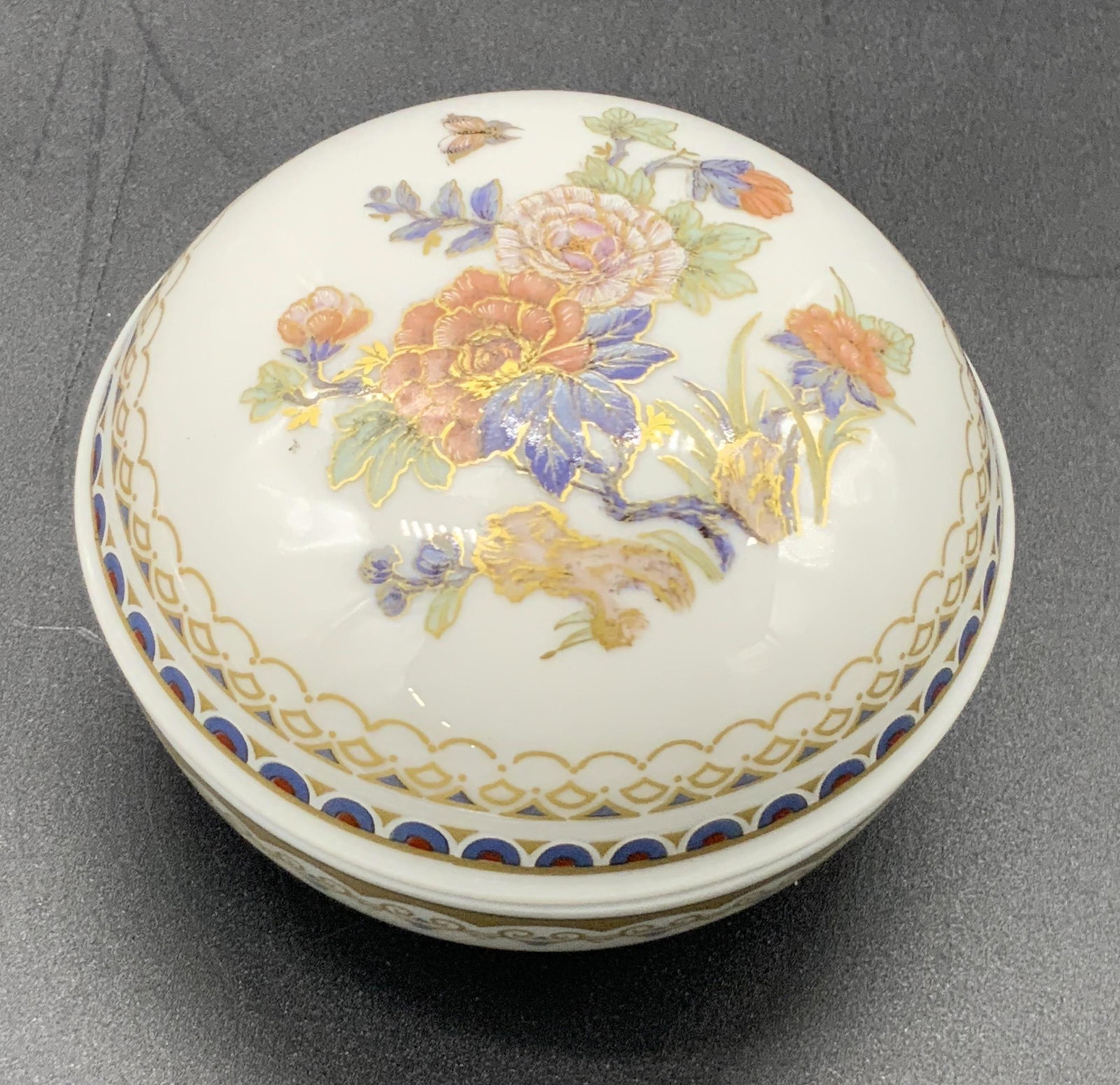 KAISER DUCHESSE German Porcelain Trinket Box, Lid: A white porcelain trinket box decorated with hand painted designs and gilt line work. The piece is circular in shape and lidded. Florals and repeating patterns decorate the entire piece. Underside is 
