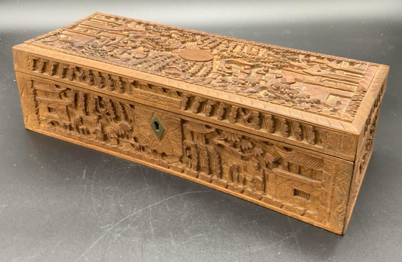 Vintage Hand Carved Wooden Trinket Box: A vintage wooden trinket box lined with a red textile. The piece features intricate hand carved designs. Wood carvings depict people in a nature setting. Keyhole and key hardware, as well as hinge har