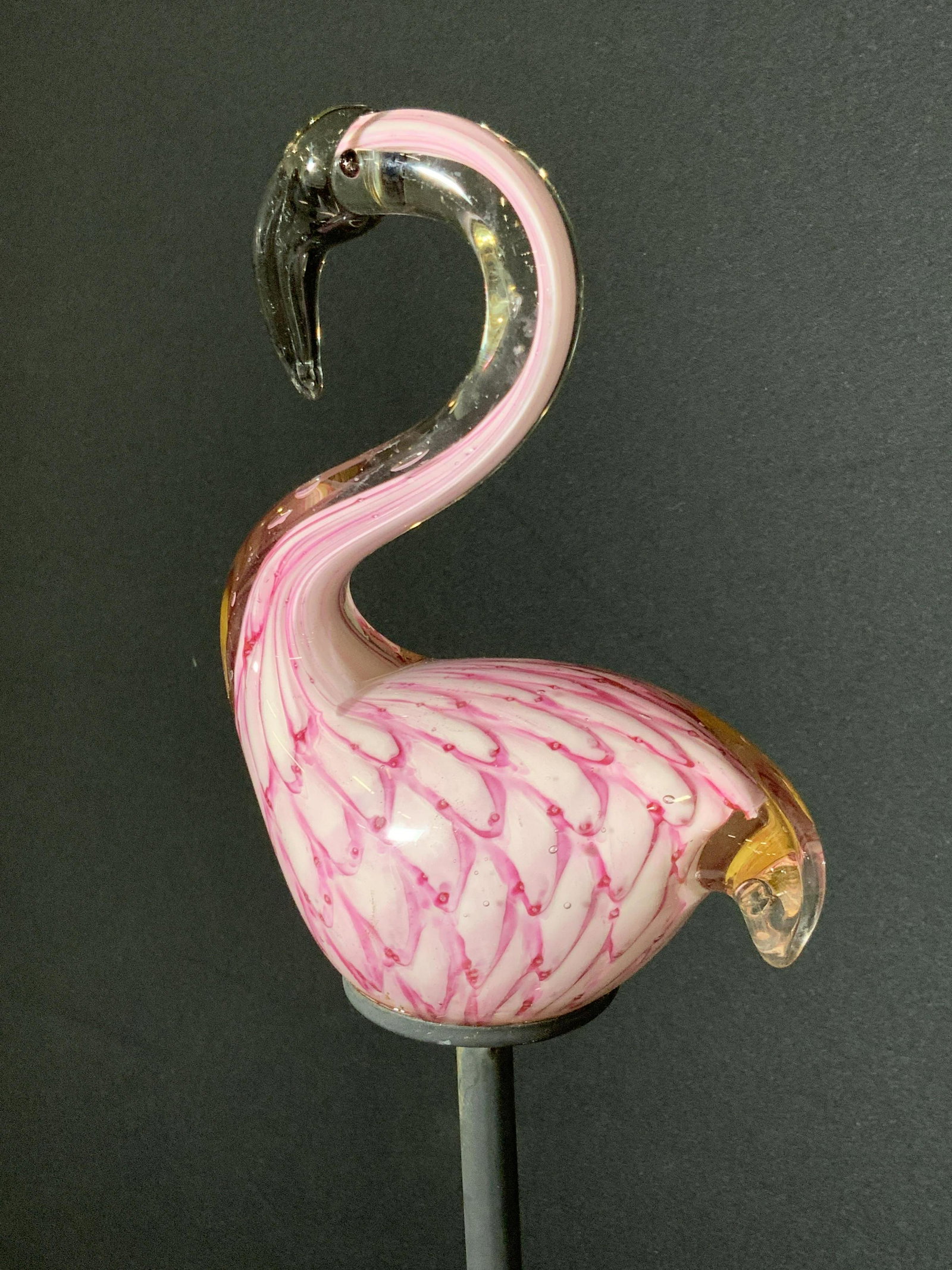 Art Glass Flamingo Lawn Ornament: A metal lawn stake with a decorative art glass flamingo topper. The glass flamingo is primarily comprised of pink hued glass and has raised black eyes. The bird is affixed to a black metal stake meant