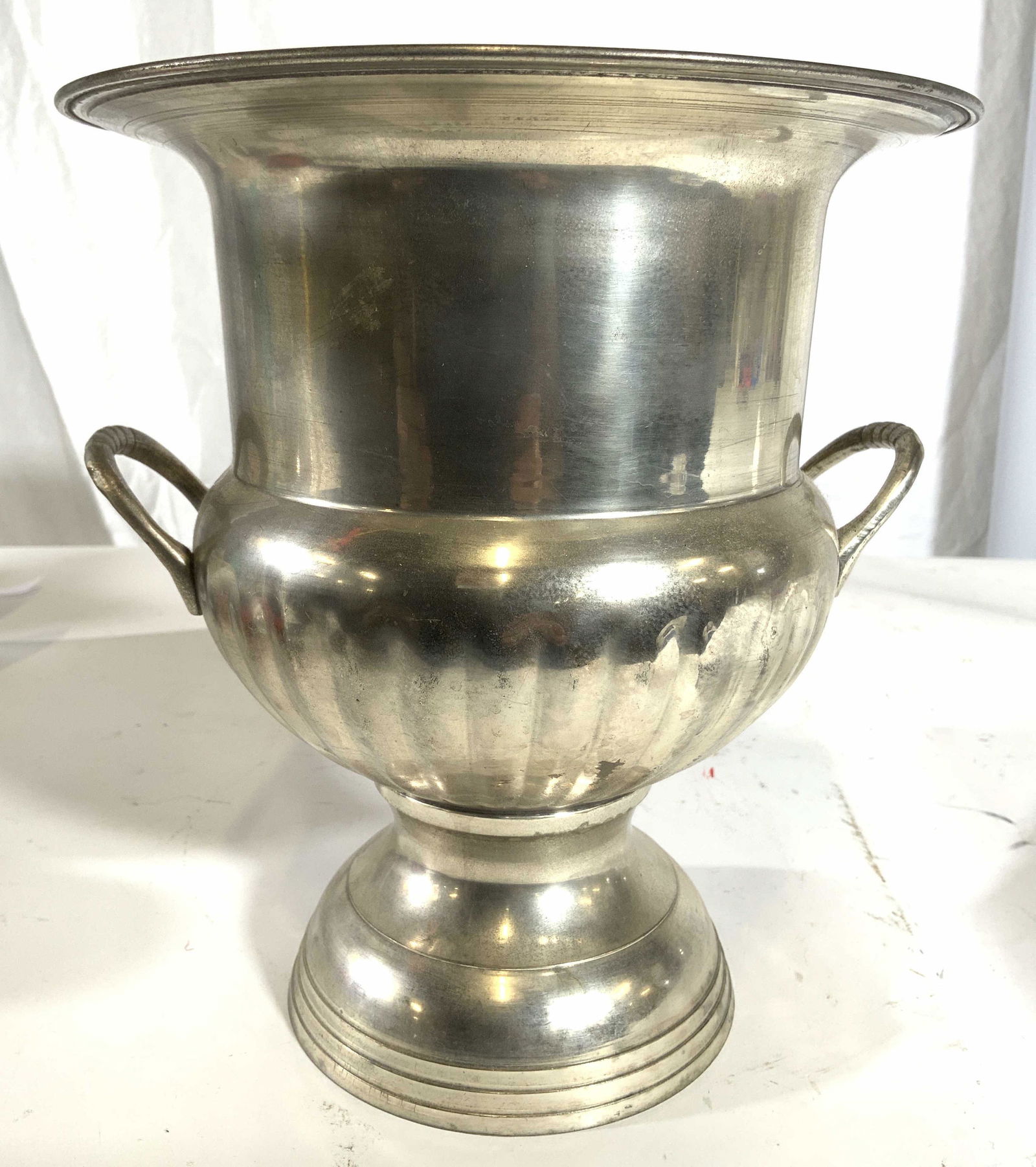 Pedestaled Handled Metal Urn Ice Bucket: Urn is silver toned and metal. Piece is pedestaled. Urn has handle on each side. Piece measures approx 9.5 inches tall 9 inches wide. Urn, ice bucket, metal urn, metal ice bucket, handled ice bucket.