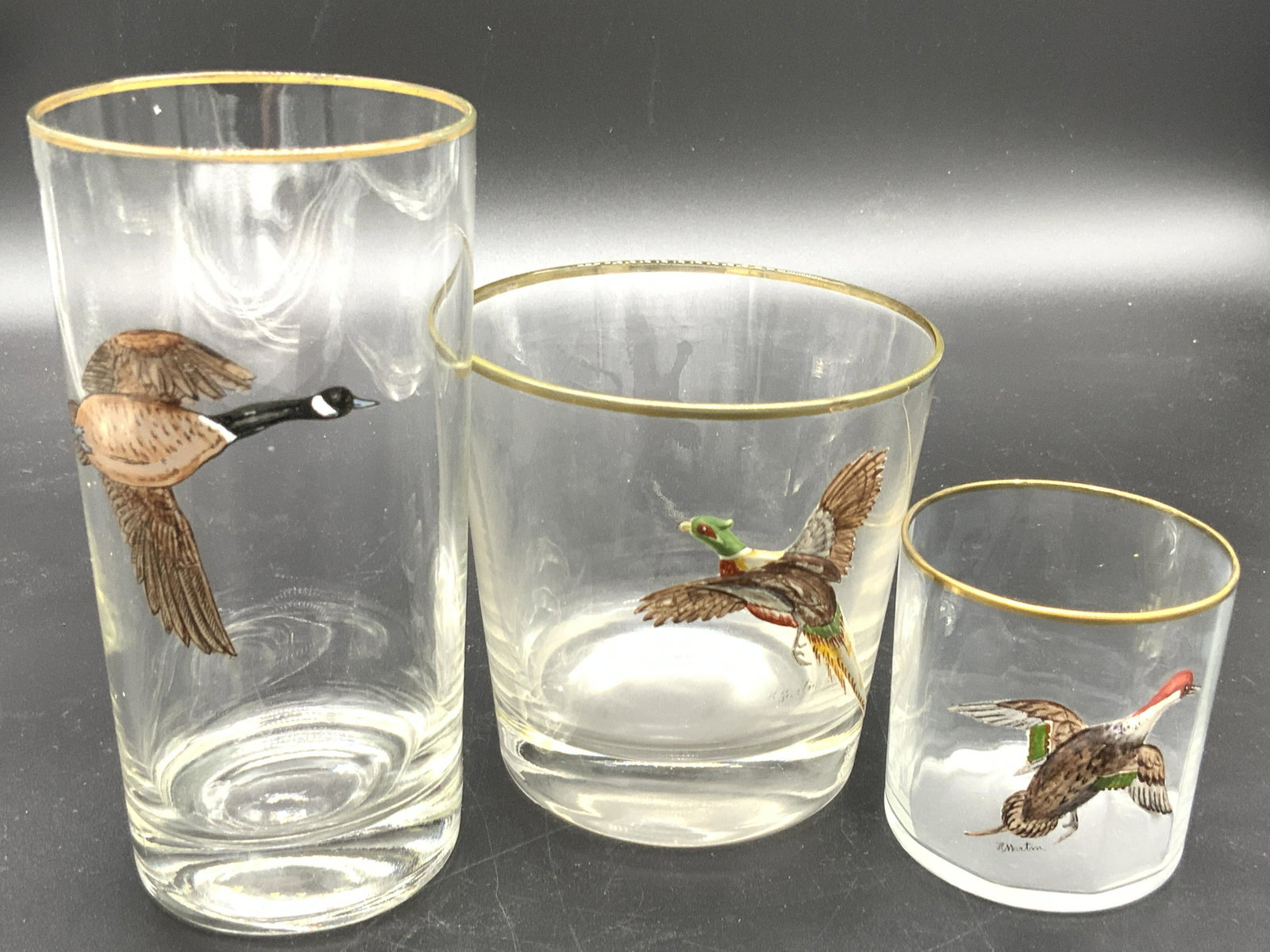Lot 3 Hand Painted Gilt Rimmed Bird Glasses: Three colorless glasses with gilt rims and hand painted birds on the front sides. Two glasses posses birds that are raised off the surface of the glass. The birds depicted are pheasants, ducks, and ge