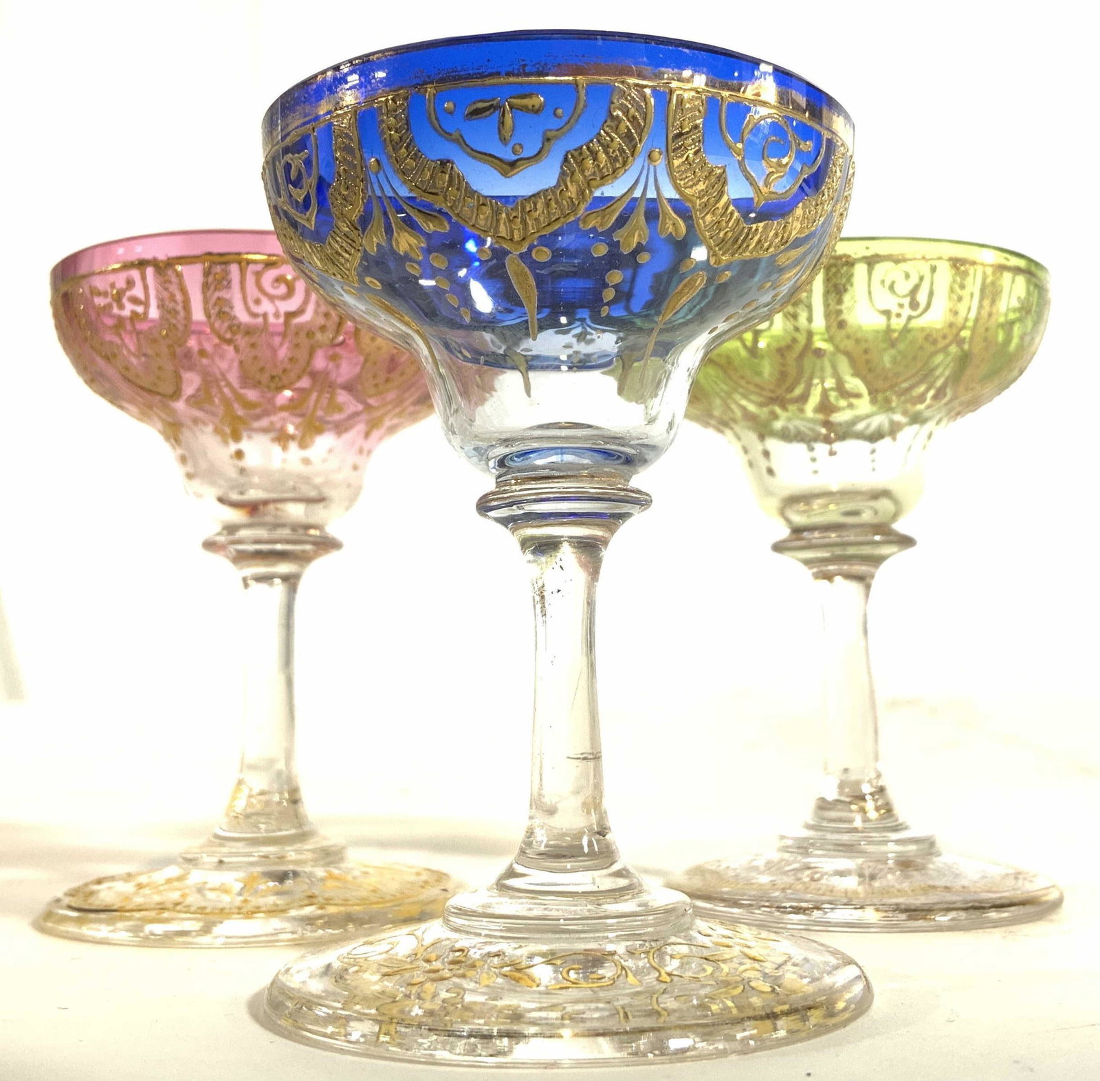 Lot 3 Petite Bohemian Glass Goblets: Lot includes 3 goblets. Each are petite in size. Includes green, blue, & pink toned goblets. Each have intricate ornate gold toned detail. Goblets measure approx 2.75 inches tall 2 inches wide. Bohemi