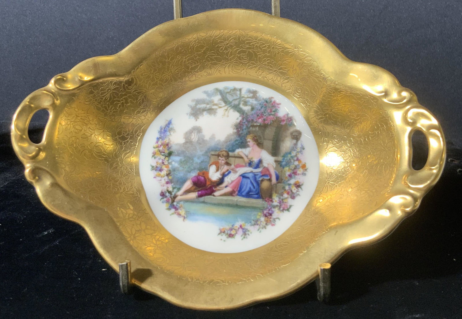 Handmade PICKARD Signed Porcelain Trinket Dish: A hand decorated porcelain trinket dish with twin handles on either end. The piece depicts a young man and woman in a nature scene in the very center. Throughout the rest of the piece, intricately etc