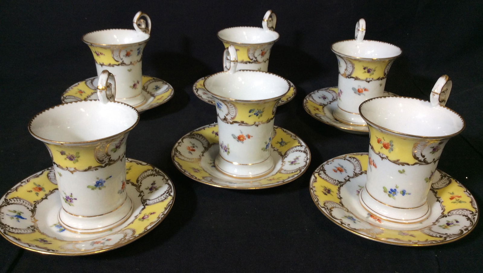 Dresden Porcelain Tea Cups & Saucers , 12 pcs: German Dresden Tea Cup Set, Setting for 6. All Hallmarked in blue ink over glaze. White porcelain with Gilt, yellow and tiny florals. Hand painted. Crack to one cup. App 3.5 in ht, saucer 5.25 in diam