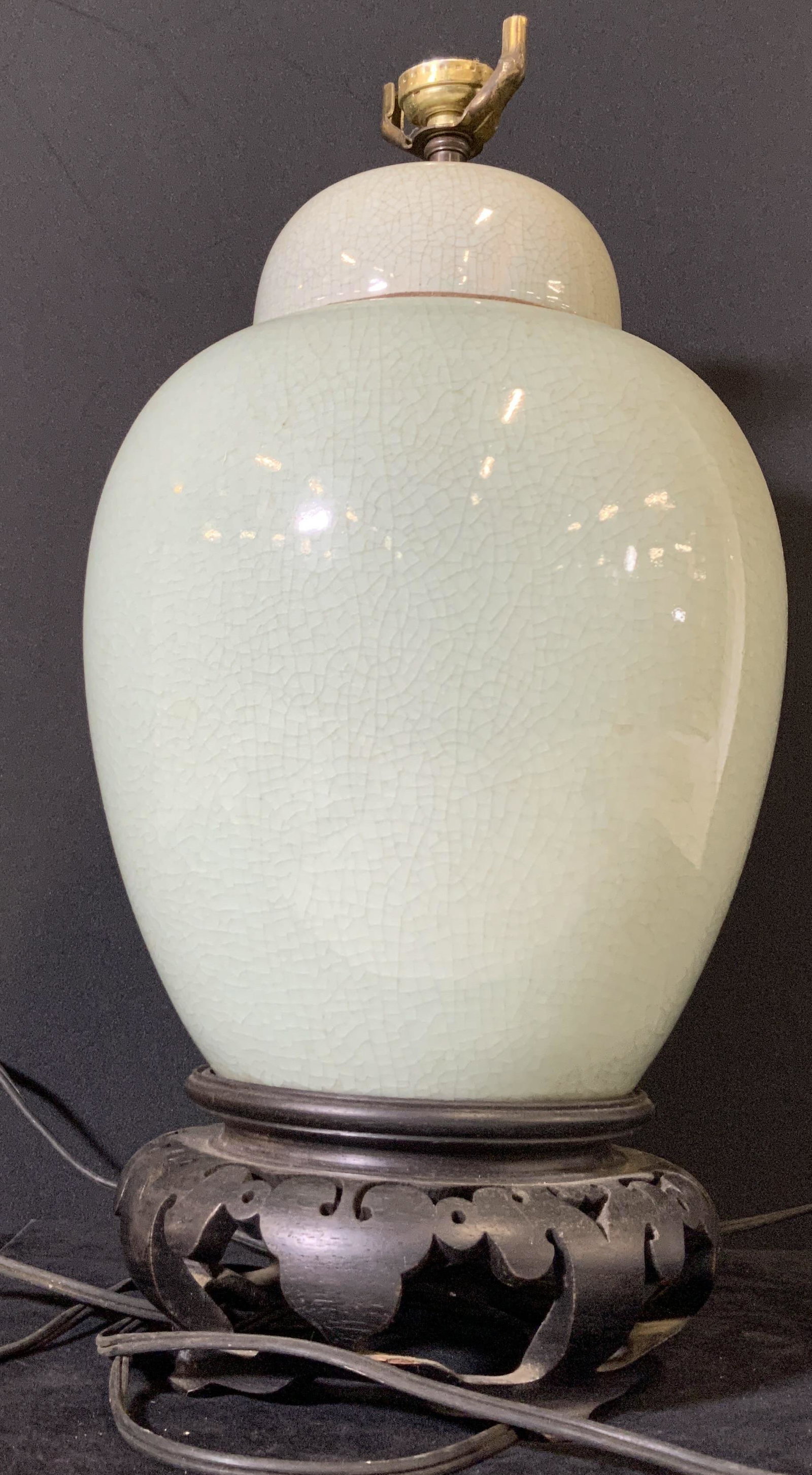 Celadon Porcelain Asian Ginger Jar Style Lamp: Green glazed Celadon ginger jar style lamp. The ginger jar sits atop a footed dark colored wooden platform. Metal hardware throughout the lighting fixture. Crazing throughout piece. Cord is long, need