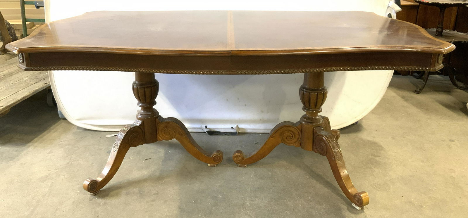 Carved Wood Dining Table w Leaves: Carved wood dining room table, includes two extension leaves. Rests on two columnar legs, each leg rests on three feet. Carved detailing decorates legs and tabletop. Multi toned wood produces an ovula