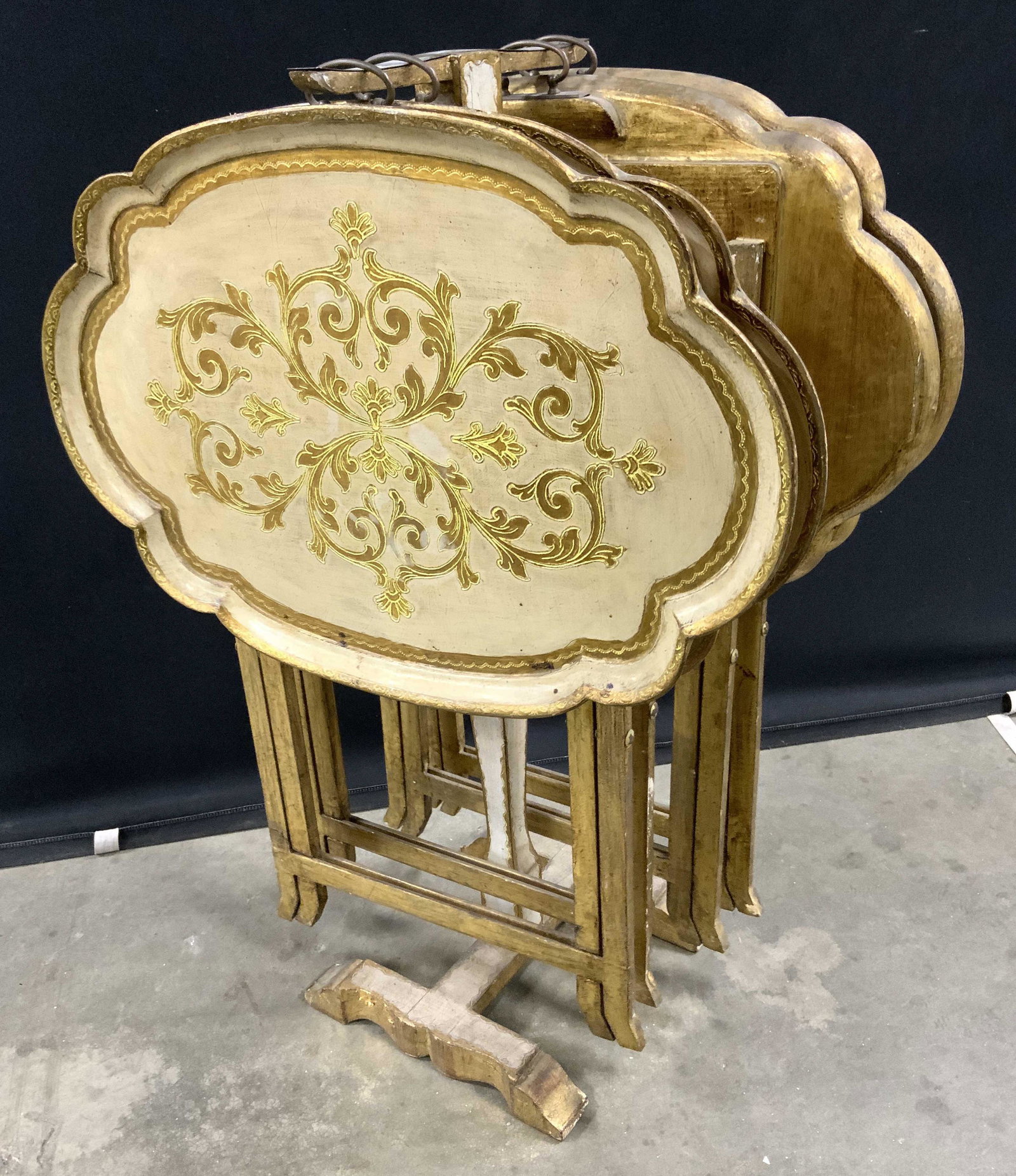 Set 5 Gilt Wood Folding Tray Tables & Stand: Lot includes 4 folding tables & 1 stand/ table holder. Table tops have ornate motif detail. Set appears to be vintage. Each table has metal hanging loop. Folding tables, vintage folding tables, gilt w