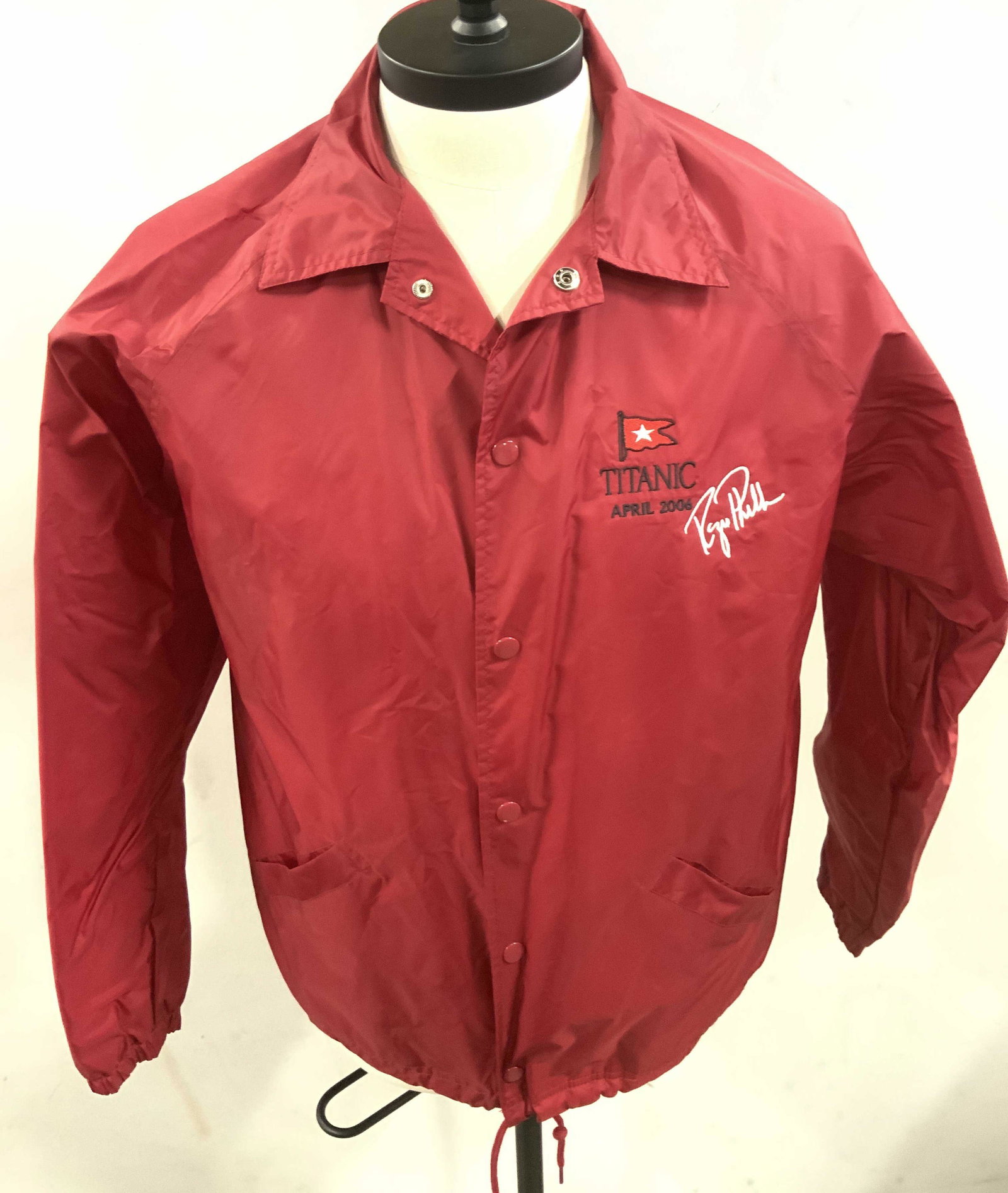 REGIS PHILBIN Sport-Tek Windbreaker Jacket: A red hued windbreaker jacket once owned by Regis Philbin. Snap button closure. Two exterior lined pockets. Piece has a patch on the obverse that reads TITANIC APRIL 2006, REGIS PHILBIN. Interior tag 