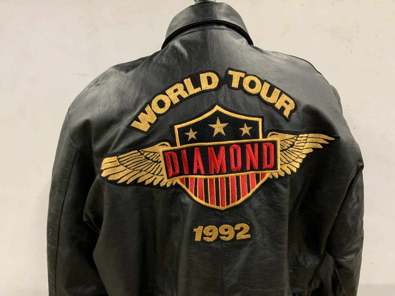 REGIS PHILBIN Black Leather Diamond Tour Jacket: A black leather jacket once owned by Regis Philbin. Primarily black with red & gold toned sewn / embroidered patches. Interior has a quilted lining. Jacket has two exterior lined pockets. One interior