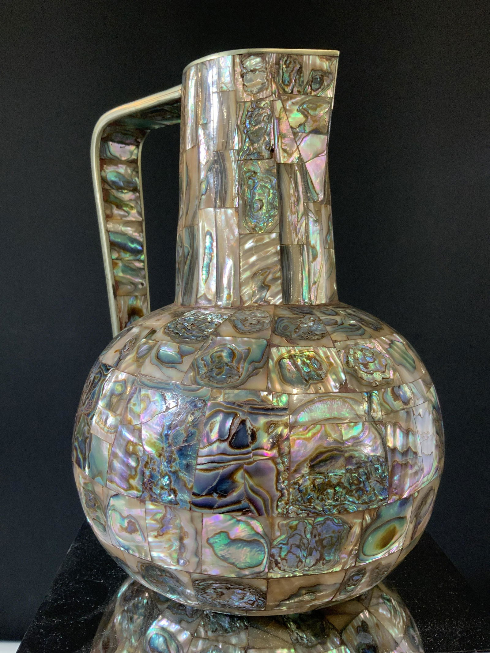 Abalone Shell Mosaic Pitcher, Mexico: Covered in tiles of Abalone shells is this pitcher, marked ‘Hecho en Mexico’ (Made in Mexico). Stands 8.5 in tall, app 7 in wide. Luxurious hand crafted item, possibly vintage, unknown white metal