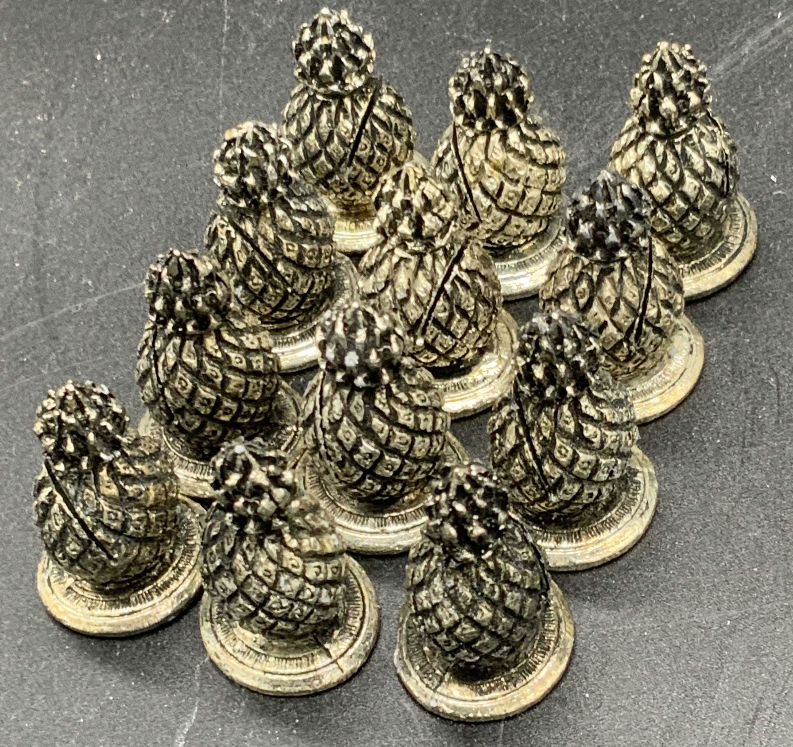 Set 12 Silver Plated Pineapple Place Card Holders: Twelve silver plated pineapple form place card holders. Each piece is etched to resemble a pineapple. There is a slit in each pineapple meant for cards. Undersides are flattened. The pieces come in a