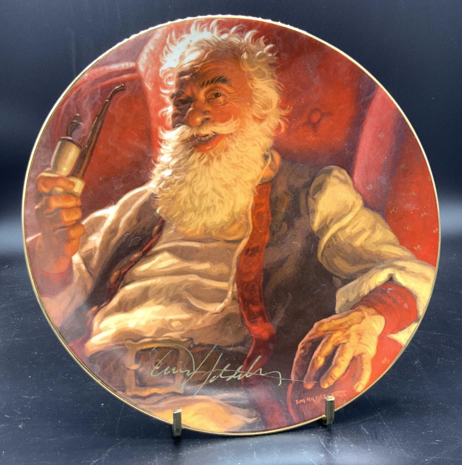 Signed LE Ceramic Santa Clause Themed Plate: A ceramic holiday plate decorated with the iconic image of Santa Clause. Beneath Santa in gilt writing reads TIM HILDEBRANDT. Beneath the gilt signature reads Tim Hildebrandt as well. Underside is sig