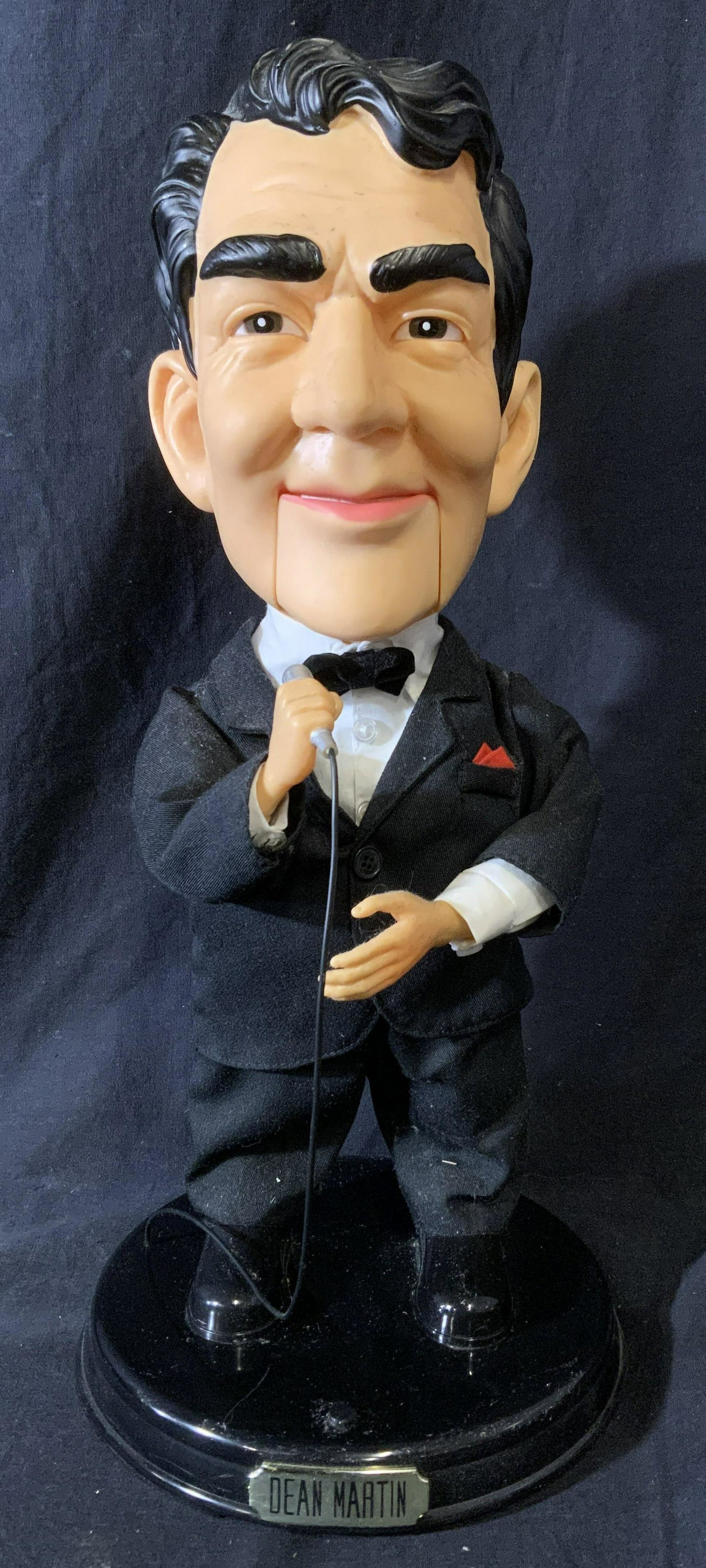 DEAN MARTIN Animatronic Figure: Dean Martin animatronic figure. Figure is mounted to a plastic base, base reads as DEAN MARTIN. Depicts a stylized Dean Martin holding a mic, and wearing a tuxedo. Measures approx 17.75 inches H, and 