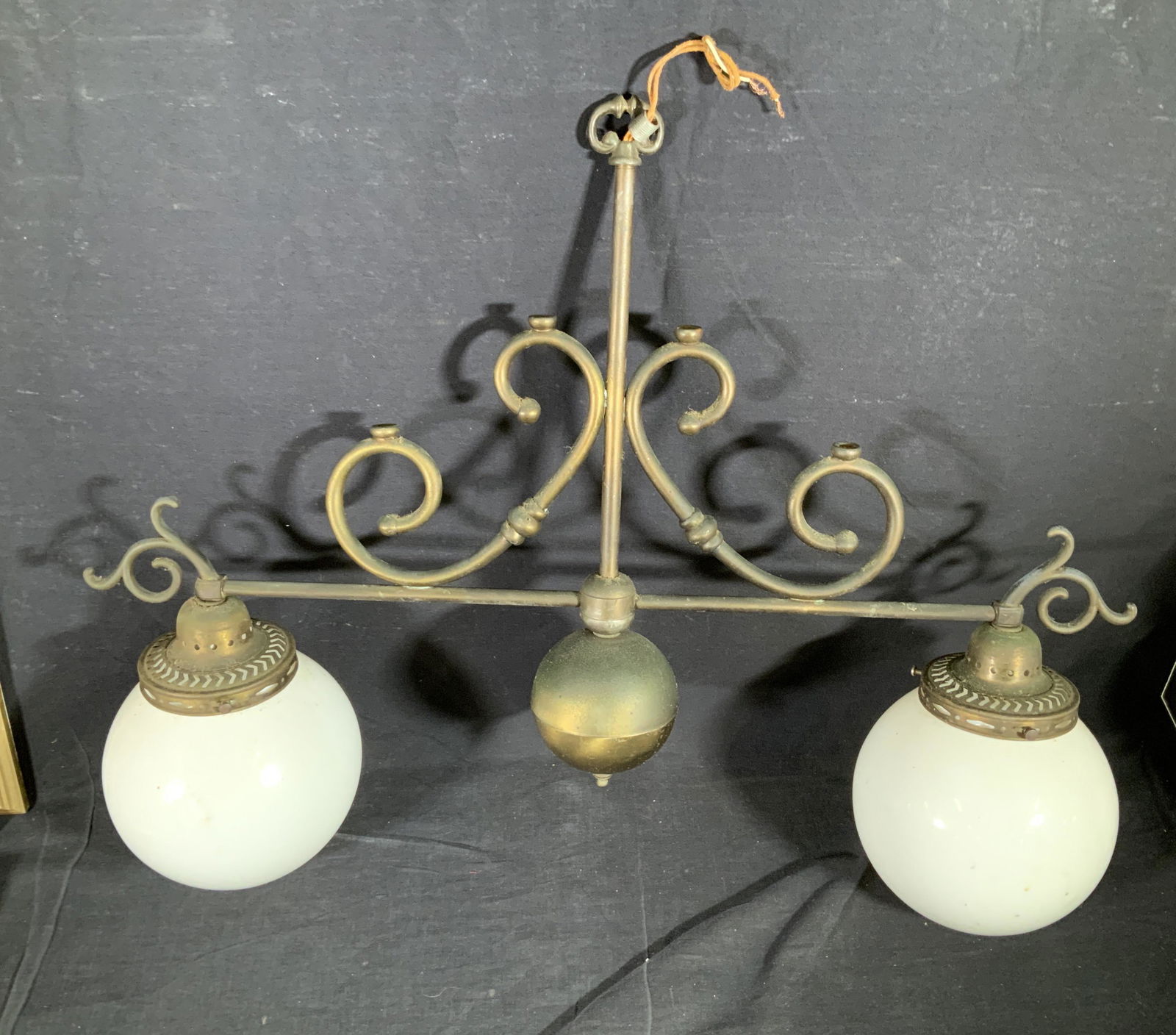 1910 Brass Dual Globe Pendant Light: Antique Bistro pendant light with two white globe shades ( milk glass globe shades) . C. Late 1890s- 1910s. Ceiling plate included. may need re wiring, upper brass scroll work in mirror image. Total w