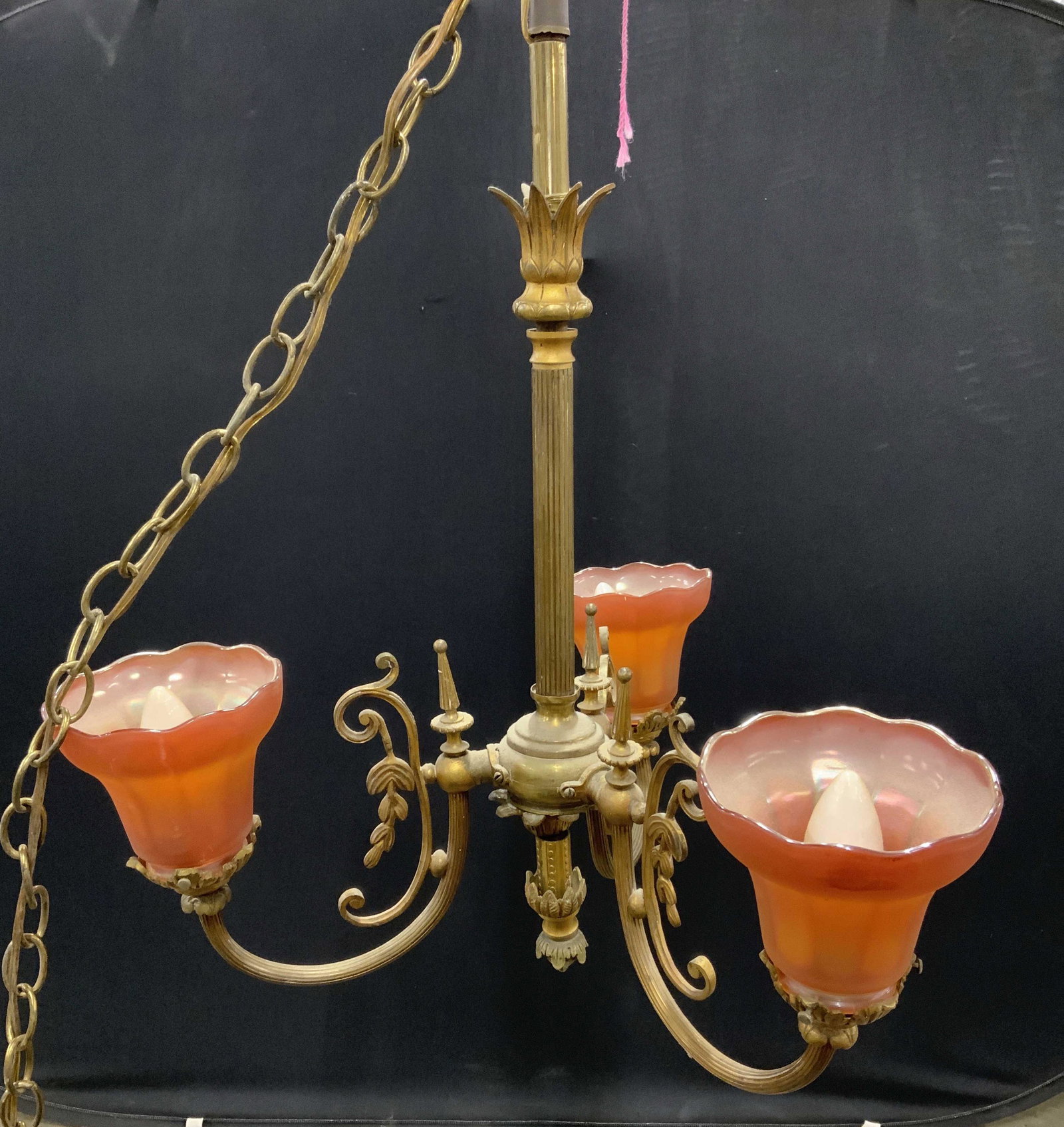 Antique Brass Chandelier W Art Glass Shades: Chandelier is vintage possibly antique. Piece is brass with 3 arms. Chandelier includes 3 blood orange toned Art glass shades. Piece has ornate c curve detail. Piece without chain measures approx 22 i