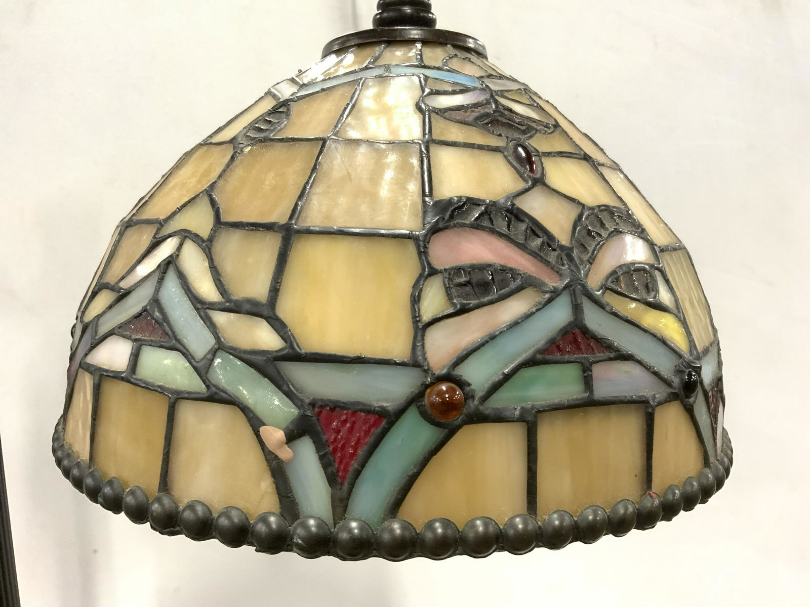 Stained Glass Shade Metal Floor Lamp: Lamp is floor size. Piece appears to possibly be vintage. Shade appears to be stained glass/ slag glass with multi toned detail. Lamp base has 4 feet. Lower end of shade has black toned studded detail
