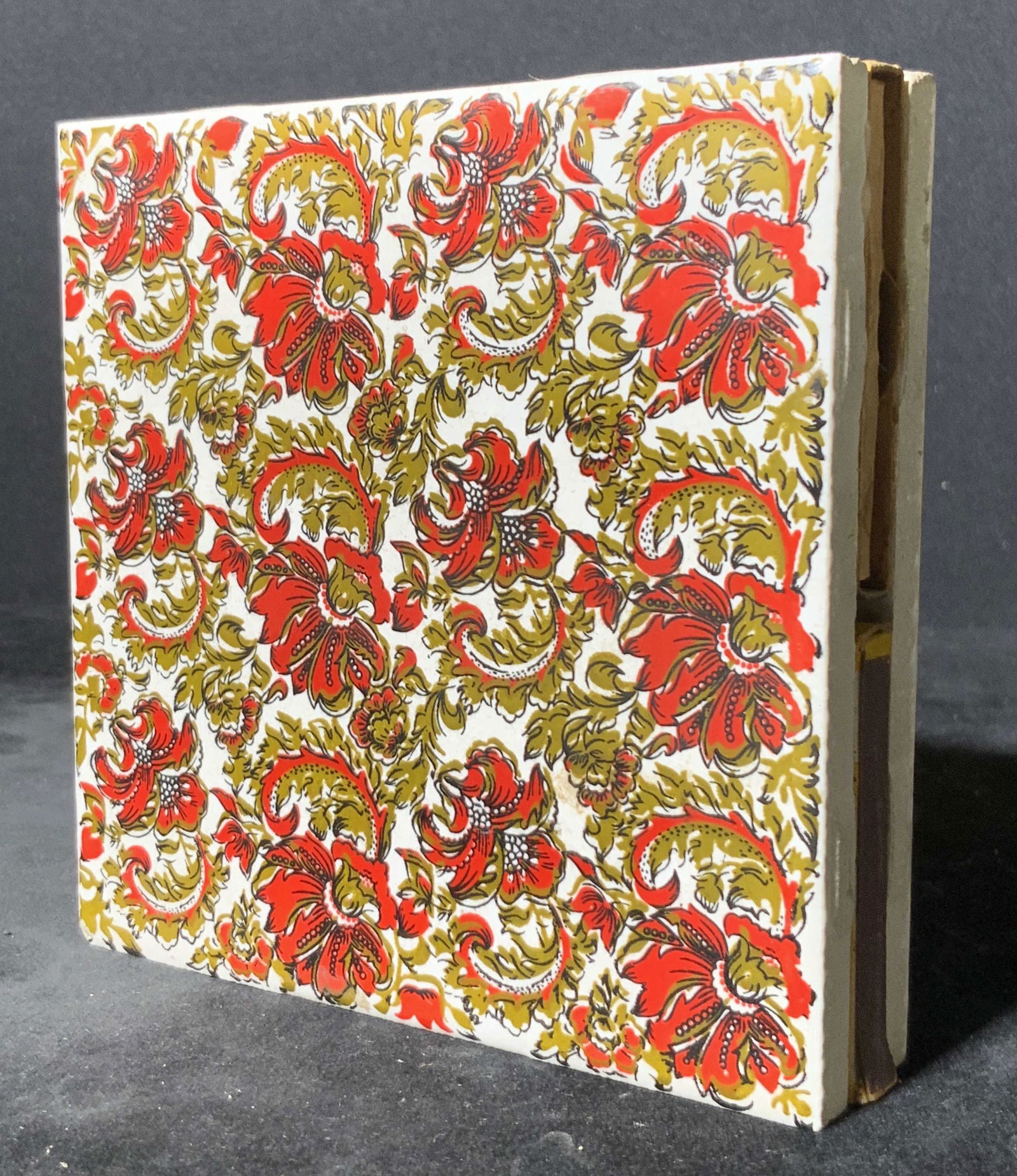 Floral Porcelain Coaster & Matchbox Holder: A white porcelain matchbox holder & coaster. The top of the piece is decorated with vibrant red florals. The underside possesses four black feet. The center features an area for storing matchboxes. Ap