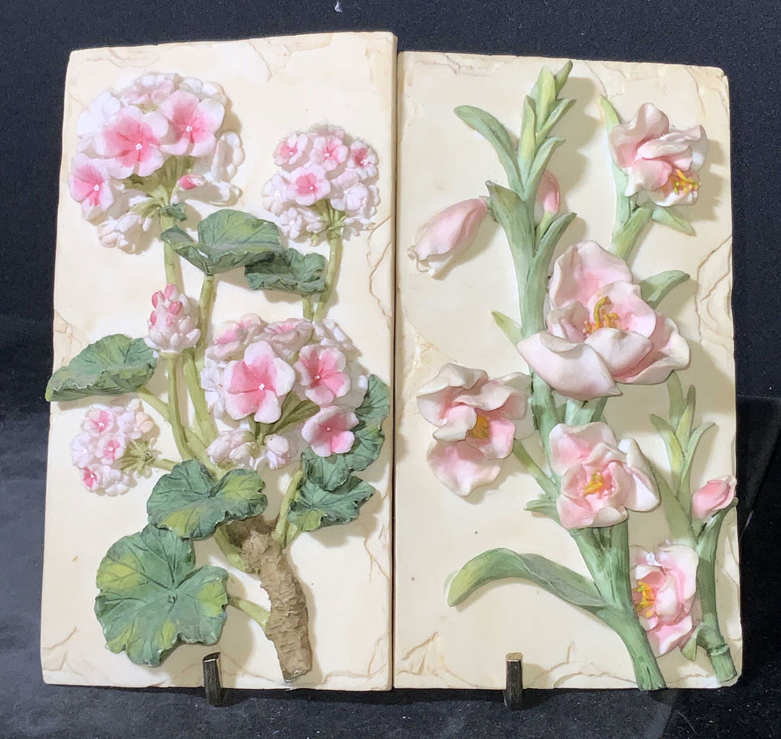 Pair Ceramic Floral Wall Tiles: A pair of pink hued floral wall tiles. The pieces feature raised florals along a beige hued backing. The undersides feature metal hardware for hanging. Approx. 6.5H x 3.5W in. Pieces have mild chippin