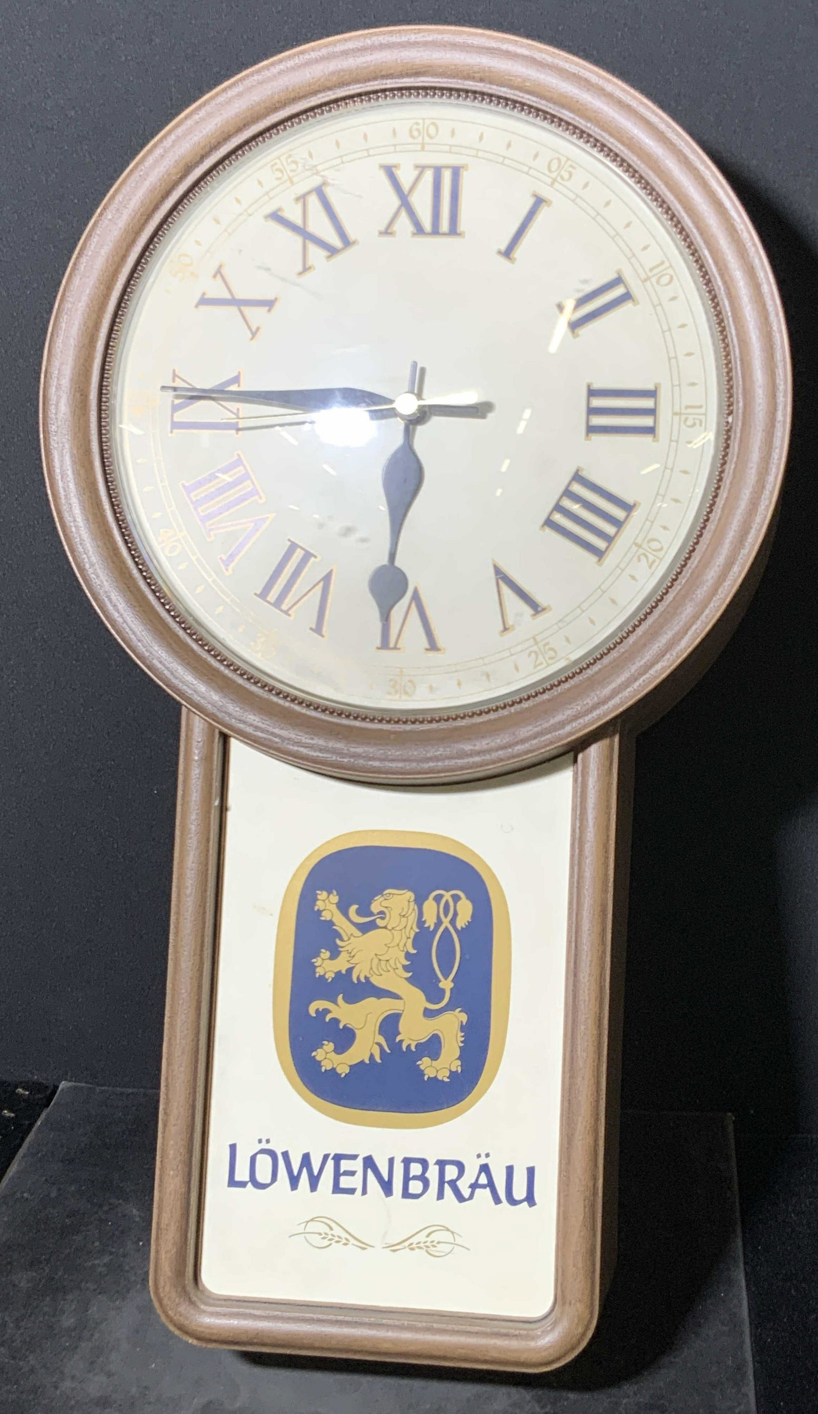 Collectible Vintage LÖWENBRÄU Wall Clock: A battery operated brown hued wall clock crafted from plastics. The obverse reads LÖWENBRÄU and depicts a mythological creature. Reverse features an area to place batteries and stickers. Stickers re