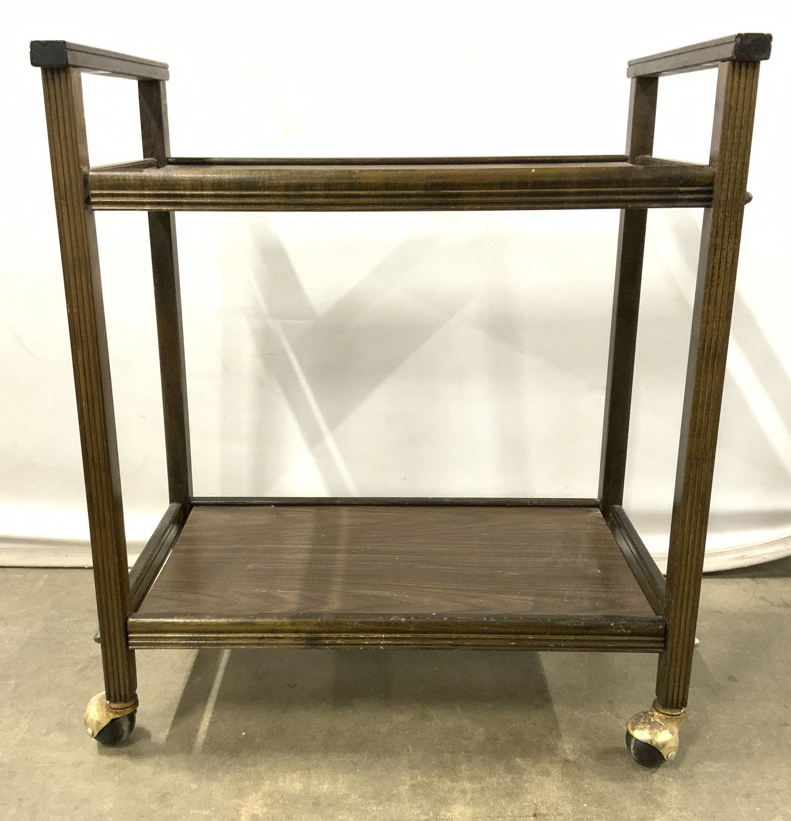 Vintage Two Tier Wooden Bar Cart: Bar cart is vintage and appears to be wooden possibly veneer. Piece has 2 tiers. Cart sits on 4 black & gold toned wheels. Piece measures approx 24 inches long 27 inches tall 14 inches deep. Bar cart,