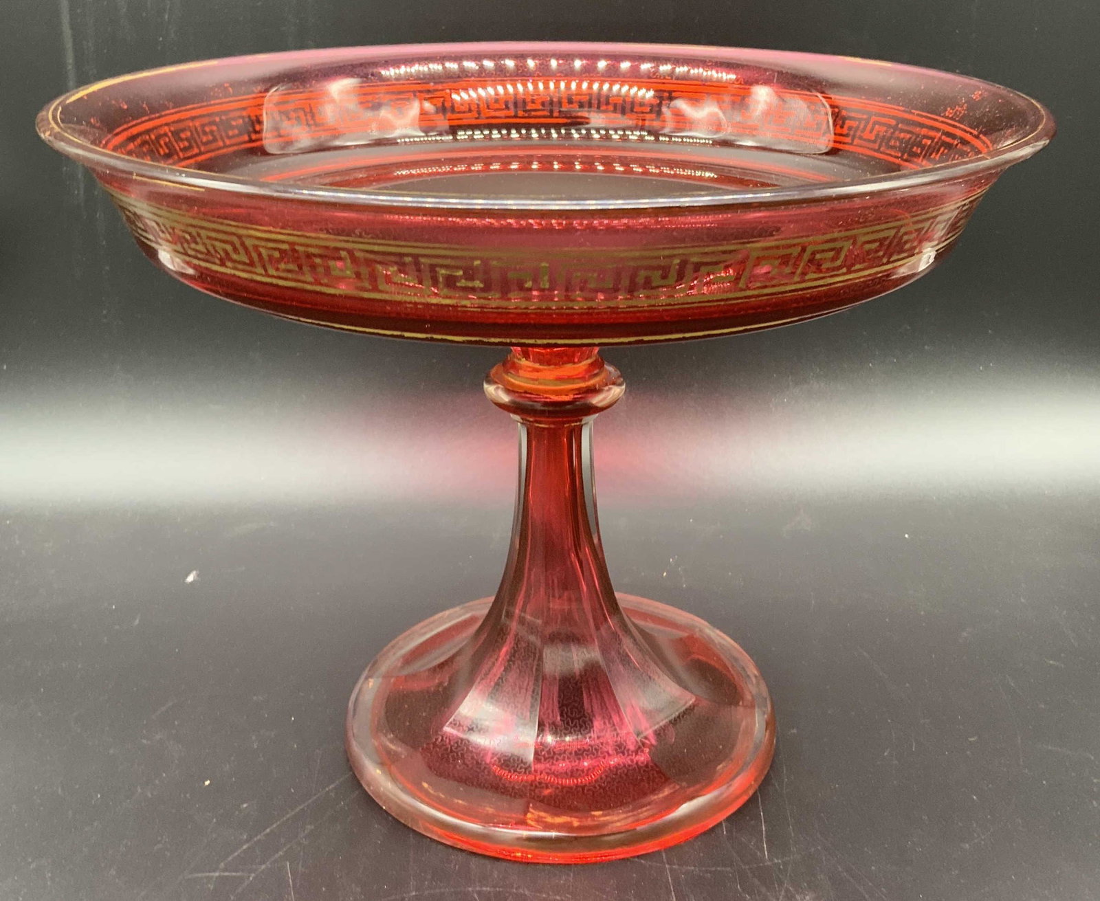 Signed Cranberry Crystal Tazza: Signed Cranberry Crystal Tazza, mark to base illegible, measures 7 3/8 inches tall x 9 5/8 inches in diameter, surface wear to piece and losses to gilt Greek key design, Signed, marked, cranberry glas