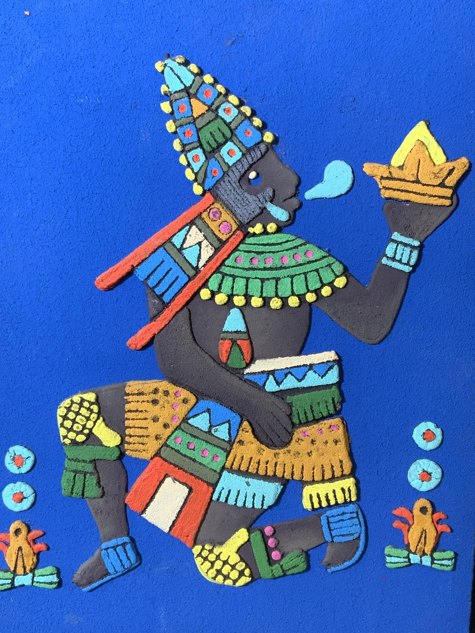 Aztec Style Relief on Board Artwork: Aztec style relief on board, no apparent inscriptions or signatures, subject a South American styled figure on a blue background, not framed, measures 16 inches tall by 12 inches wide, chips and wear 