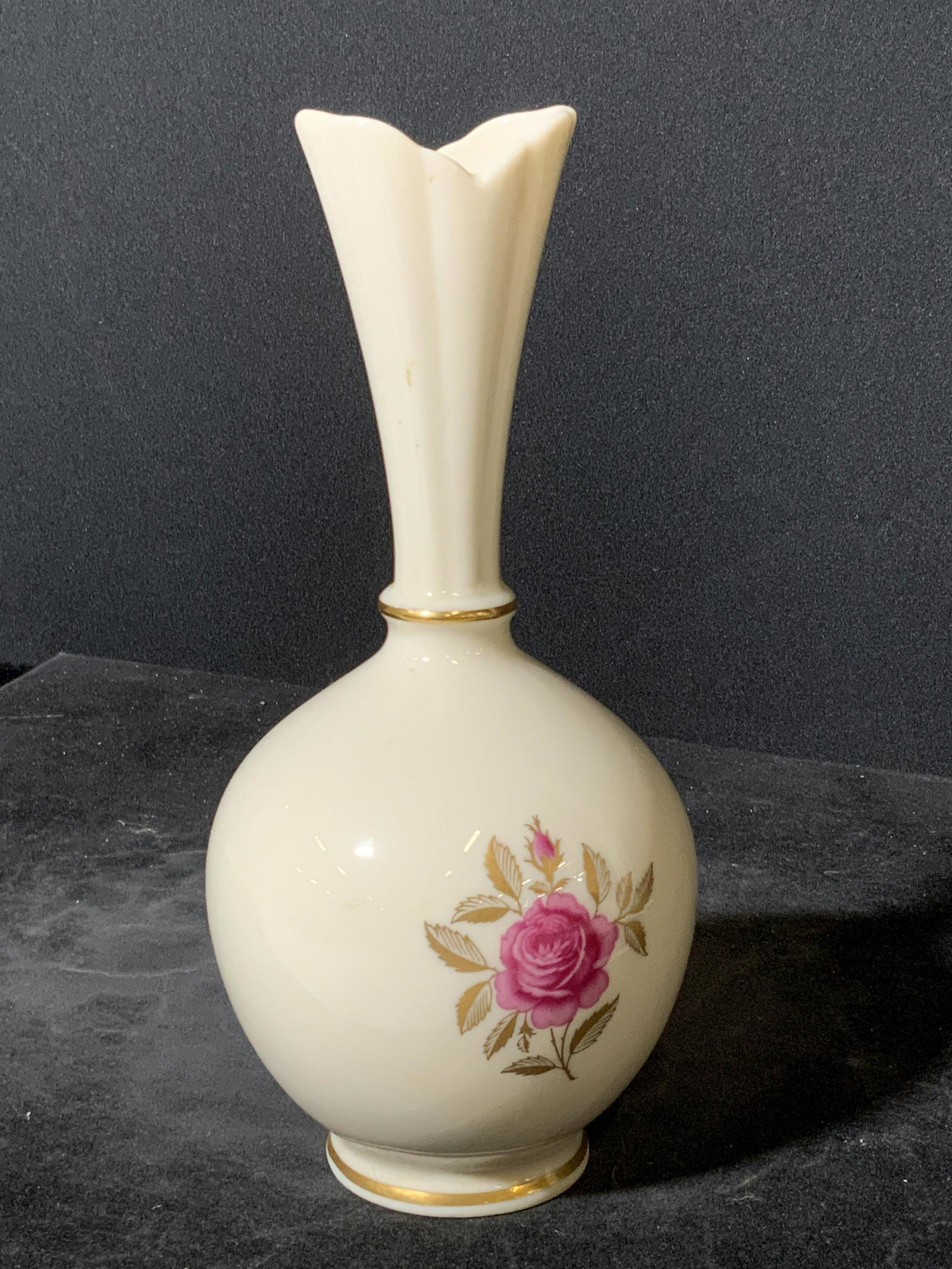 LENOX Signed Floral Porcelain Vase: A white porcelain vase with gilt line work and a pink hued floral accent in the center. The neck of the vase features embossed porcelain designs. Underside signed LENOX, MADE IN USA. Approx 8H x 3W in