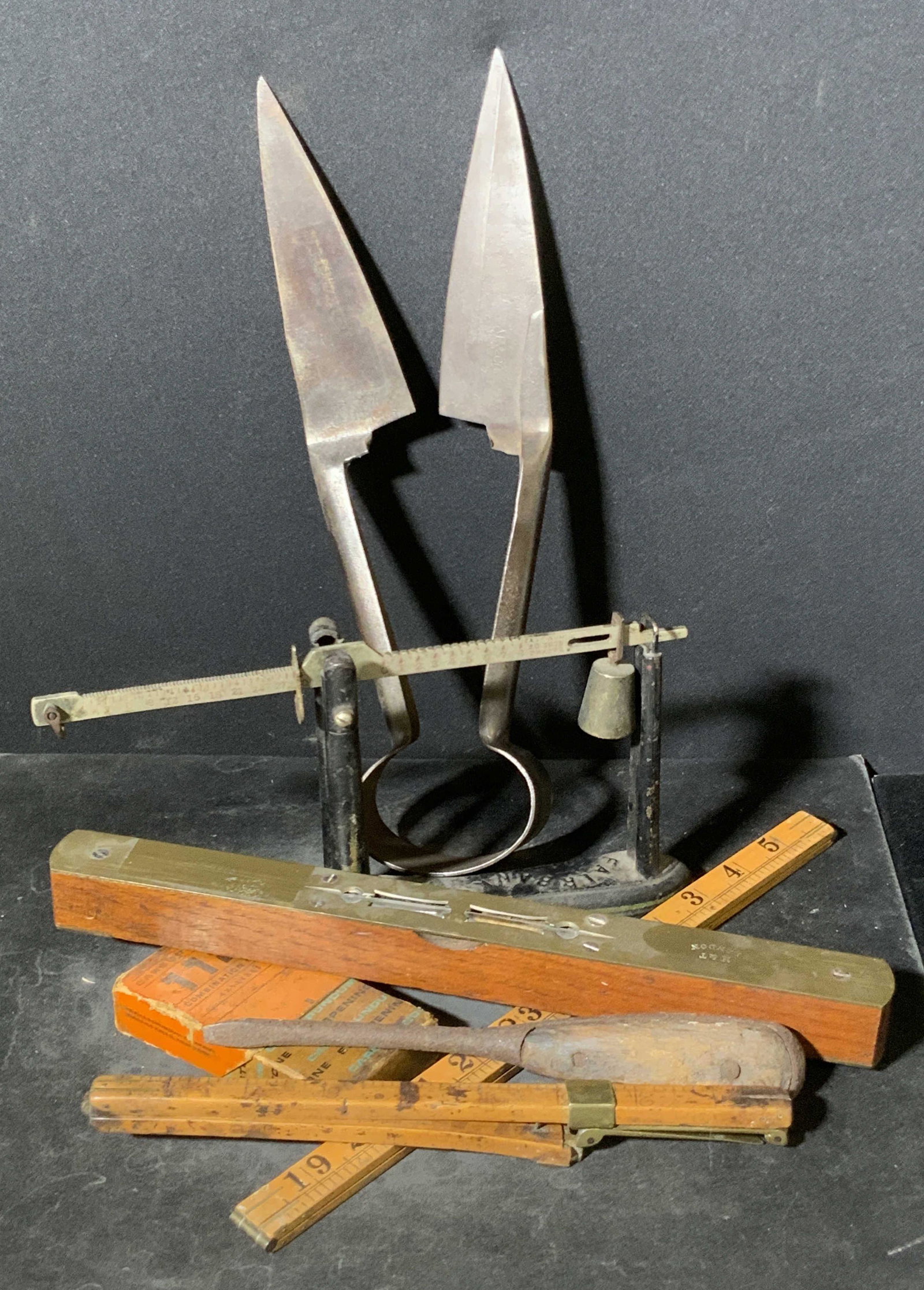 Lot 7 Antique & Vintage Collectible Tools: Seven vintage and antique tools once used form performing household tasks. Lot includes rulers, a level, a sharpening stone, shears, a screw driver, and more. Pieces are crafted from metal, wood, and 