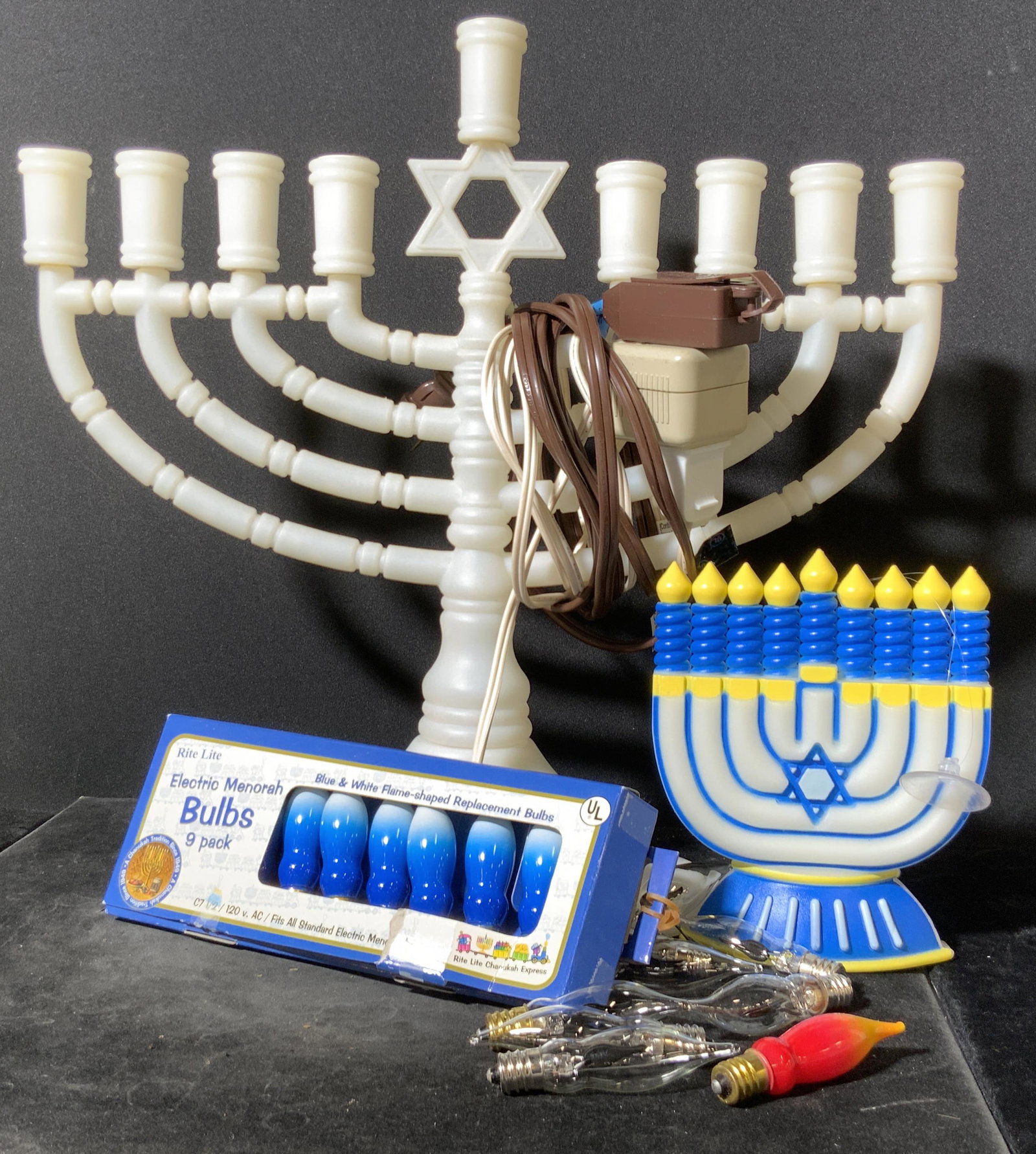 Lot 2 Composite Lighted Menorahs, Judaica: Two composite lighted Menorahs. Both pieces are crafted from composite materials. Primarily white hued in color, one has blue & yellow accents as well. The larger piece functions with lightbulbs. Some