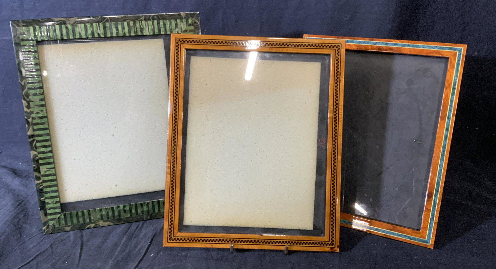 Lot 3 Marquetry Picture Frames: Lot of 3 vintage picture frames. Decorative detailing accomplished through marquetry. Largest measures approx 12 inches H and 10.25 inches W. One of the frames is decorated with a teal print resemblin