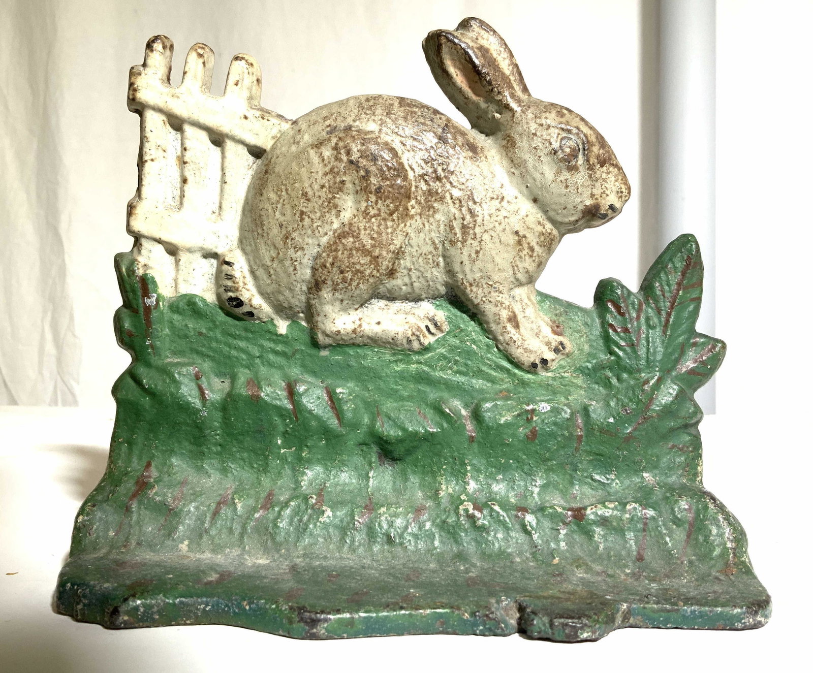 Antique Iron Rabbit In Grass Figural Doorstop: Doorstop is vintage possibly antique. Piece appears to be hand painted. Depicts a rabbit near a fence seated in leaves & grass. Piece measures approx 6 inches tall 7 inches long 3 inches deep. Doorsto