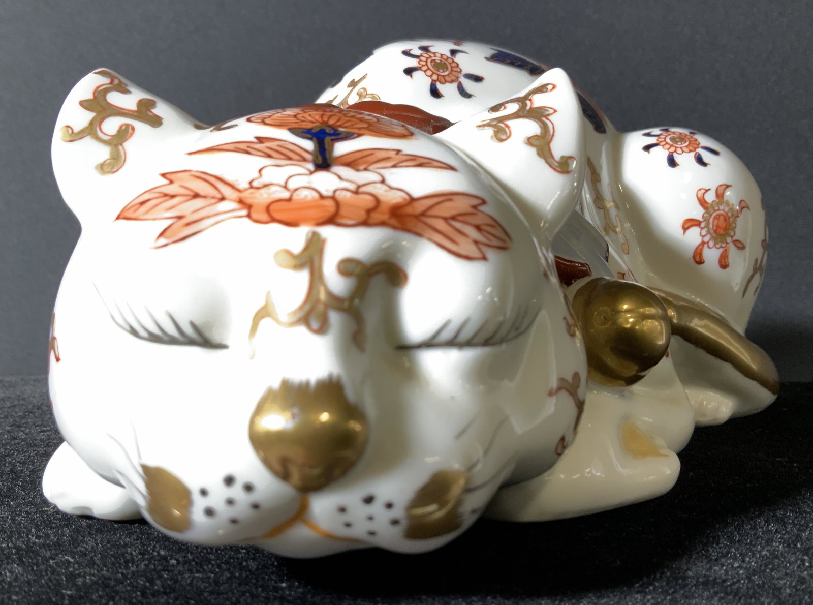 Imari Style Signed Asian Porcelain Cat: Sleeping White Porcelain Cat, delicate eye lashes. Imari Pattern and Patina of orange , blue and gilt. Solid gilt tail. Underside signed Asian Characters. 9.5 in long, 5 in wide. Asian Decorative Arts