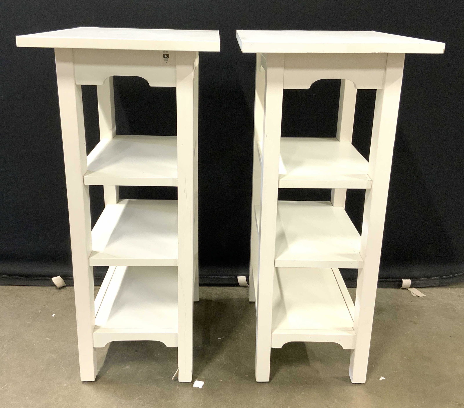 Pair White 3 Tier Side Tables End Tables: Lot includes 2 side tables. Each are white toned and appear to be wooden possibly veneer. Tables each have 3 shelf tiers including lowest shelf. Each measures approx 30 inches tall 19 inches deep 14 i