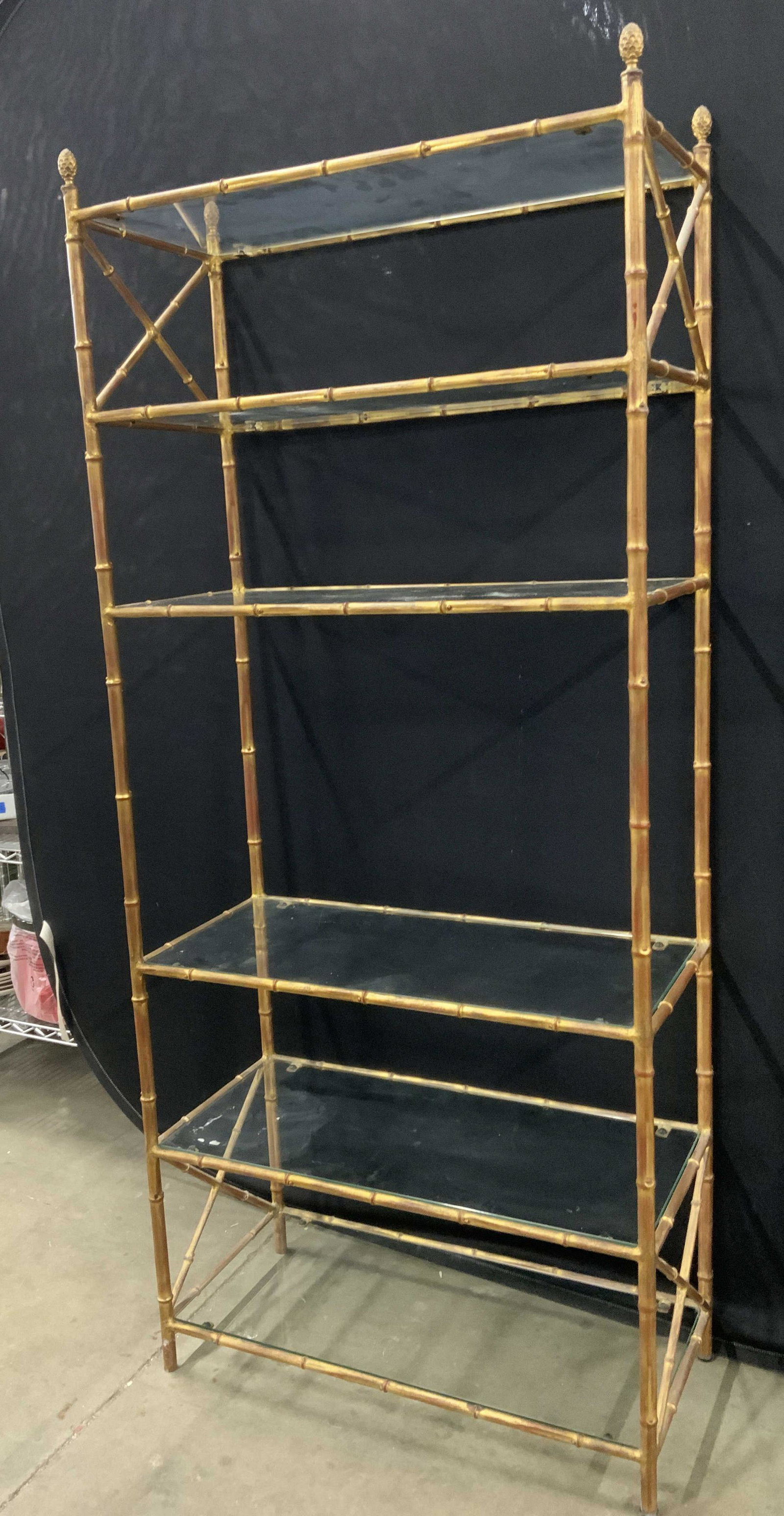 6 Tier Metal Display Shelf W Glass Inserts: Display has 6 tiers. Piece is metal, appears to possibly be vintage. Each tier includes glass insert. Top of piece has 4 finials. Top and lower area have x shaped structures. Shelf appears to be gold 