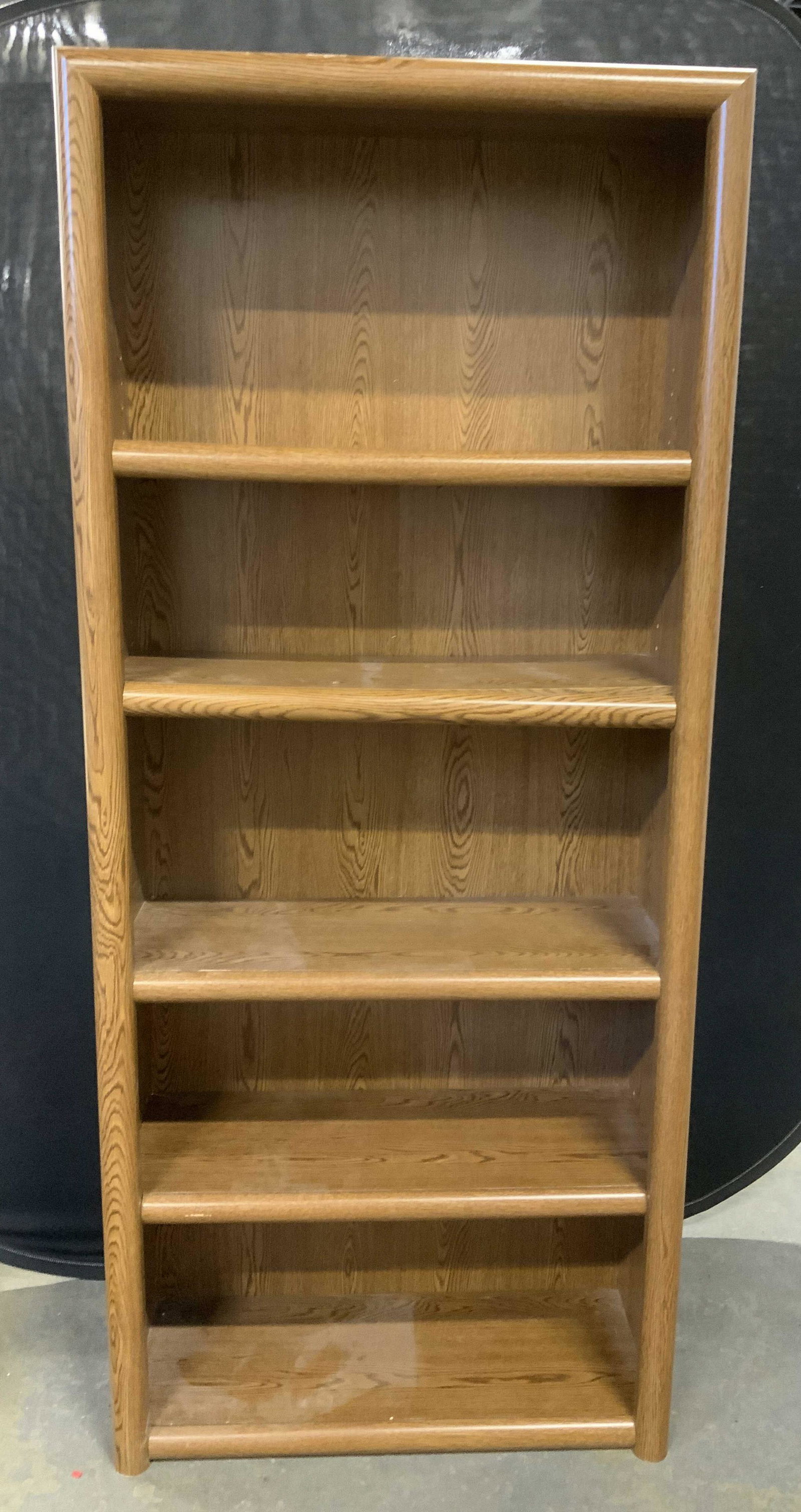 Veneered Wooden Book Shelf: Wooden book shelf, finished with a veneer. The four shelves are adjustable. Some warping to shelves, trim on one of the shelves has loosened and needs to be reattached. Brackets affixed to top of case