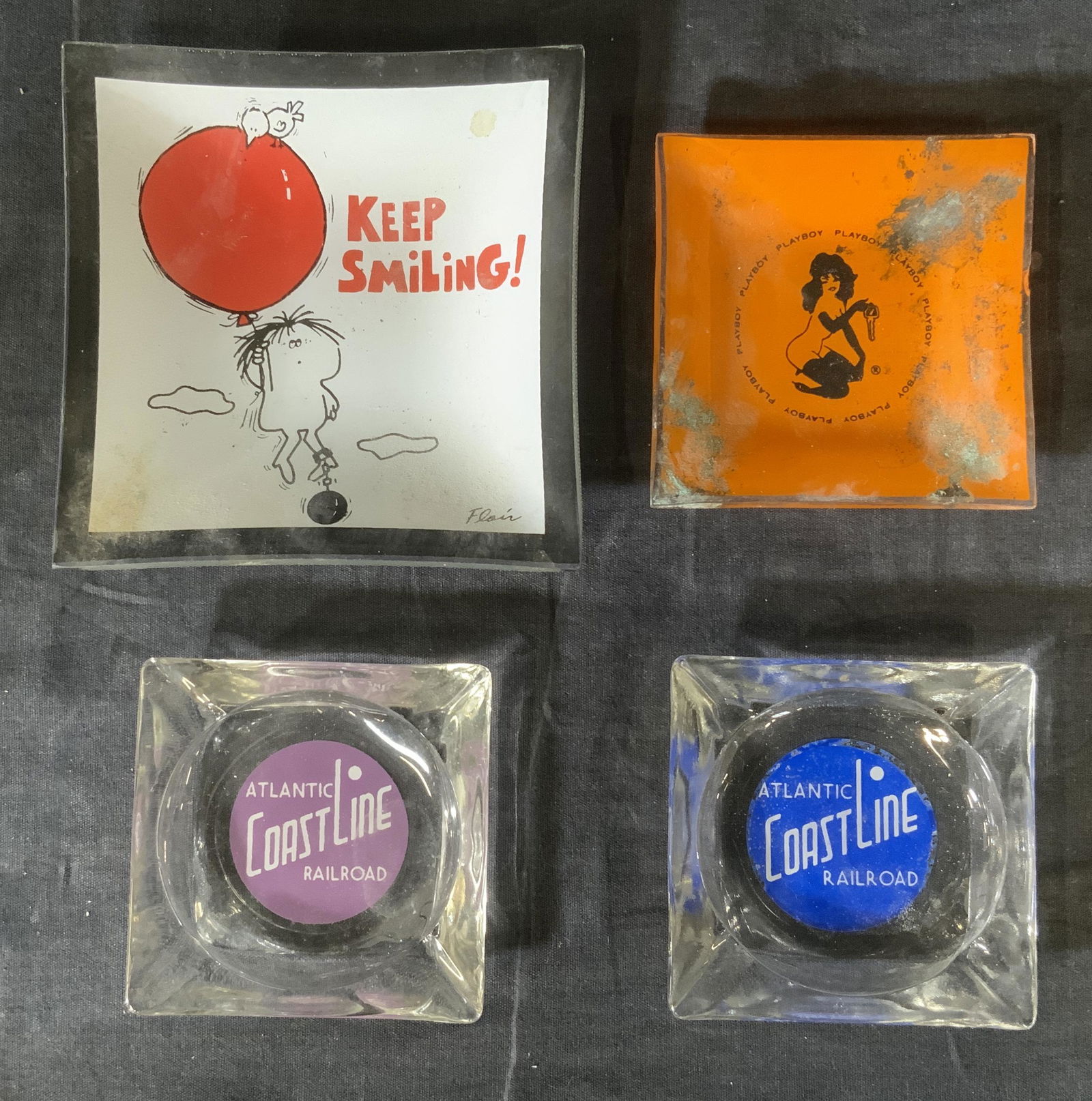 Lot 4 Vintage trinket dishes Ashtrays: Lot 4 Vintage Ashtrays, inscriptions read ‘Keep Smiling’, ‘Playboy’, and ‘Atlantic Coastline Railroad’, smaller dishes measures 3 1/2 x 3 1/2 inches, largest dish measures 5 1/4 x 5 1/4 in