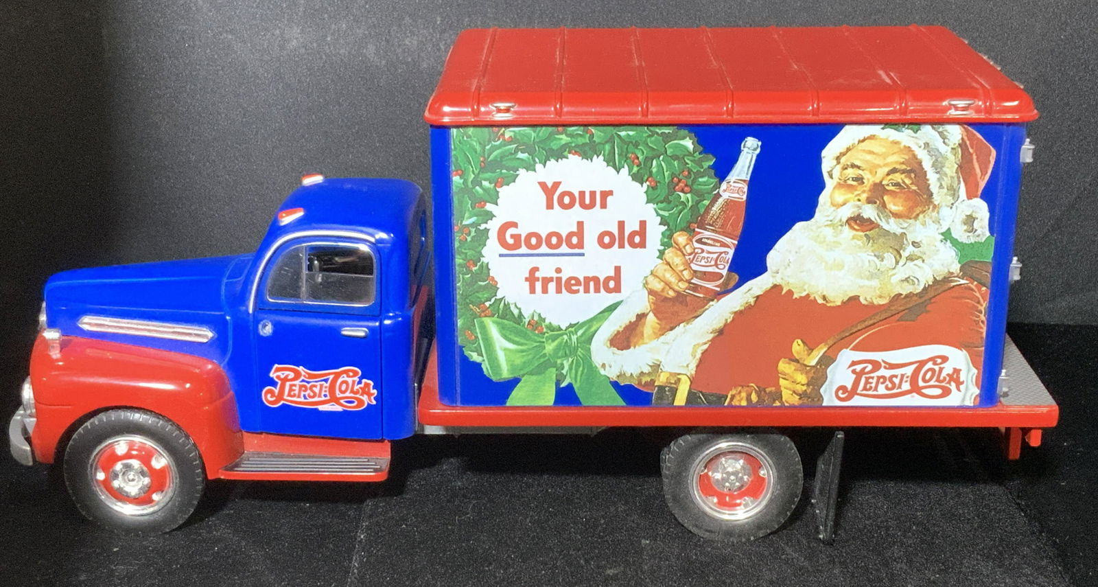 Collectible PEPSI COLA Holiday Toy Truck: Metal Toy Vintage Pepsi Cola Transport Truck with Image of Santa Claus holding a glass Pepsi Cola Bottle. Advertisement Holiday truck reads ‘Your Good Old Friend’ inside a holiday wreath. Backside