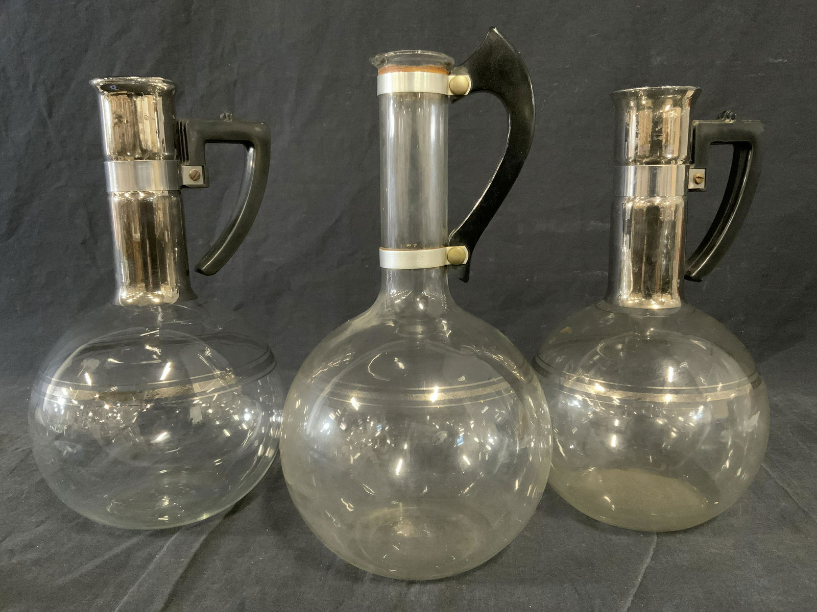 Lot 3 Blown Glass Coffee Decanters: Lot includes three decanters, one is marked PYREX, possibly vintage. Lids are absent. Bodies are decorated with silver striating, two decanter necks are colored silver. Largest measures 12.5 inches H,