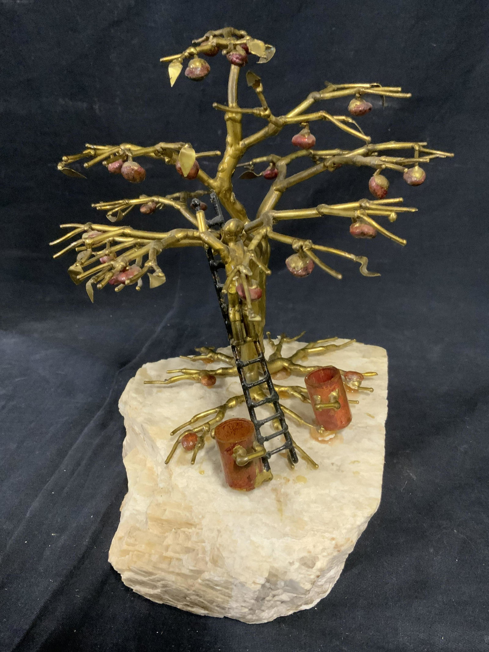 Apple Picker Metal & Stone Sculpture: Metal sculpture, possibly vintage. Depicts a person picking apples. Tree and figure appear to be crafted from brass, apples, and buckets are possibly stone or colored glass, base is stone. Measures ap